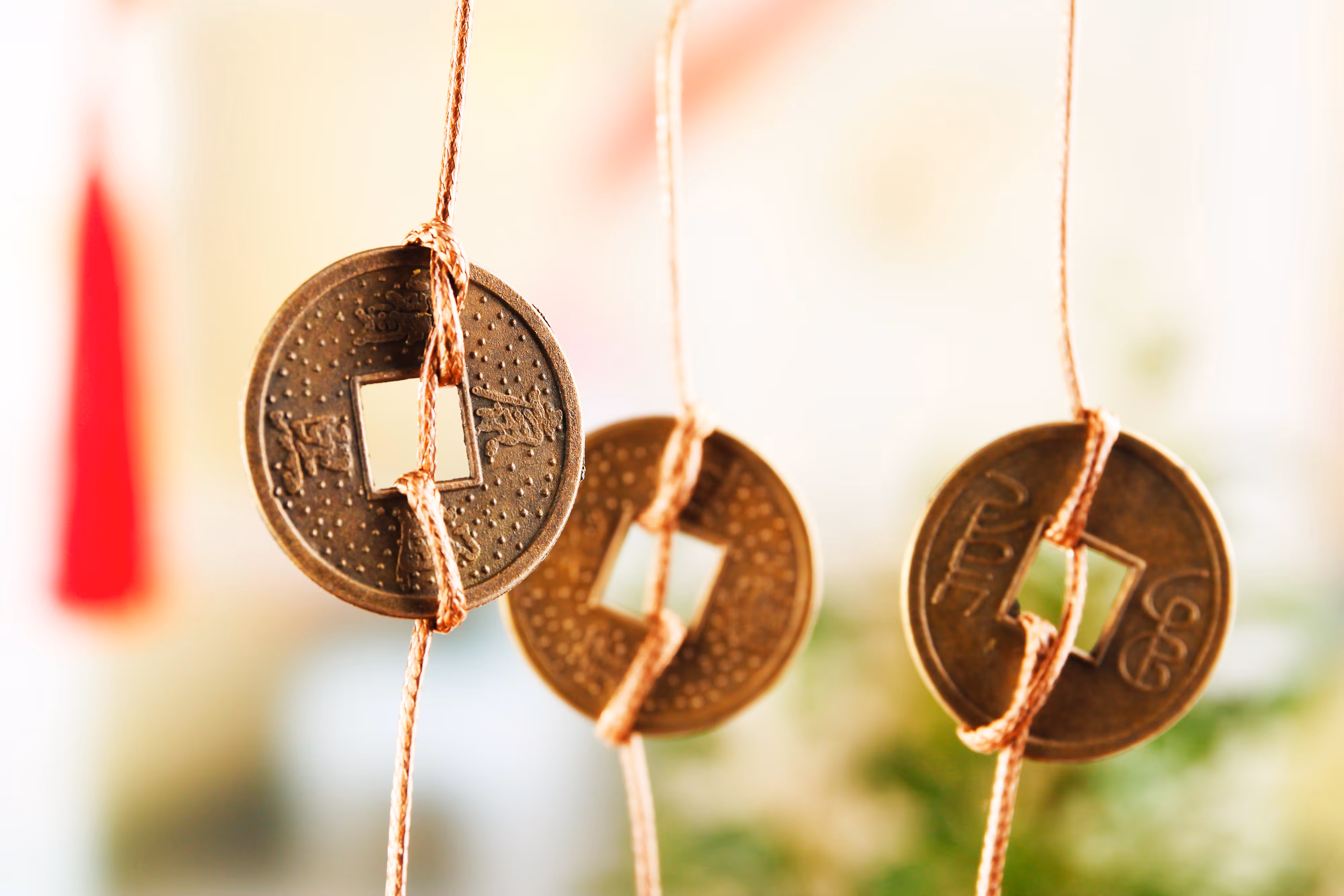 Three ancient Chinese coins with square holes in the center, tied with brown strings and hanging against a blurred background.