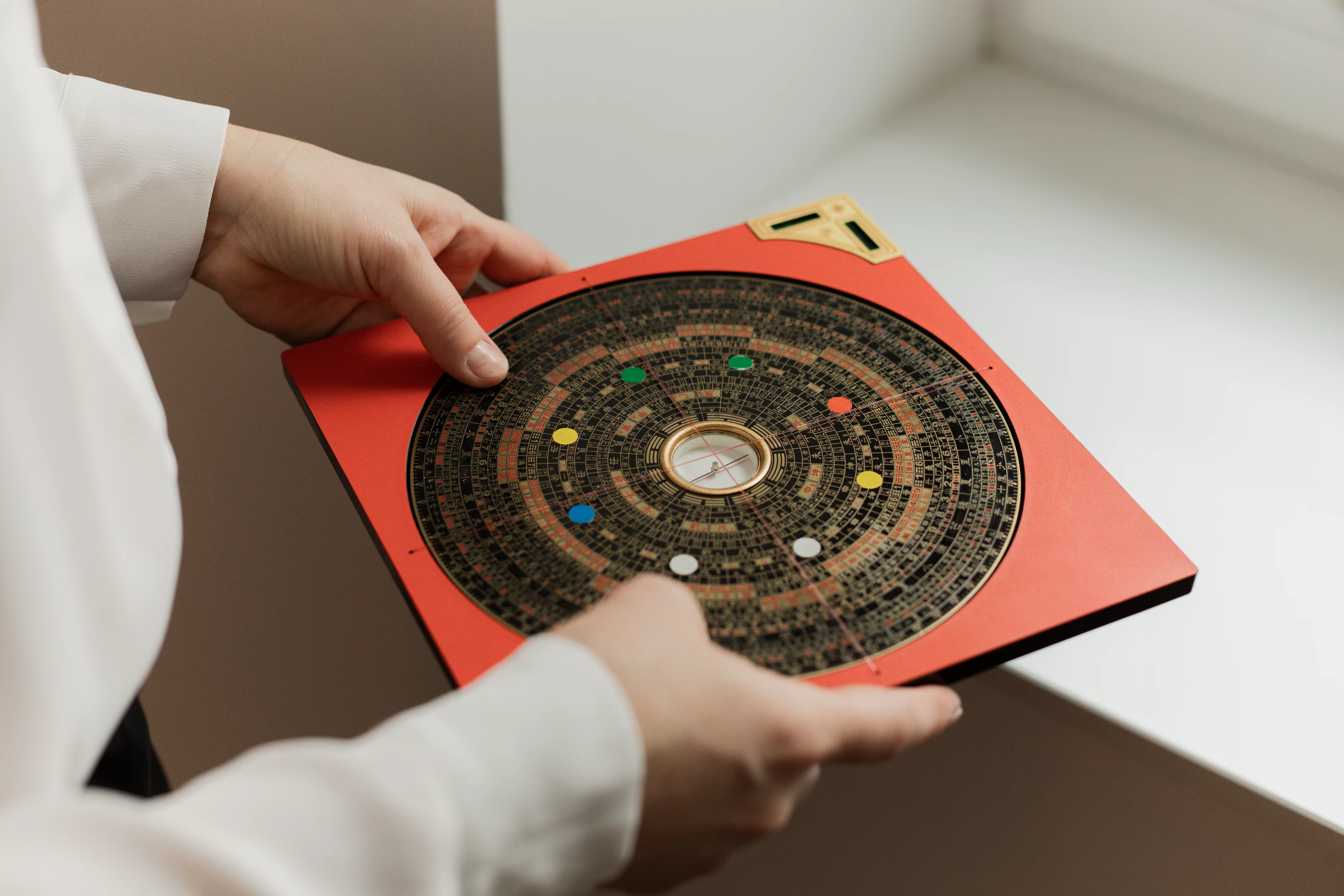 A person holding a traditional Chinese feng shui compass with a red square base and multiple concentric circles of symbols and markings.