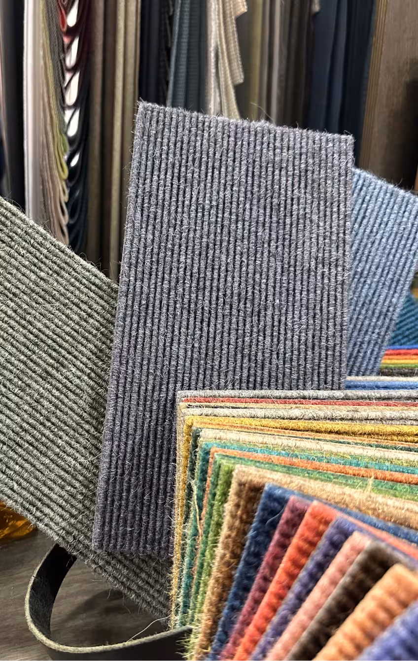 Close-up view of various fabric swatches with ribbed textures in multiple colors including gray, green, blue, and earth tones, arranged in overlapping layers.