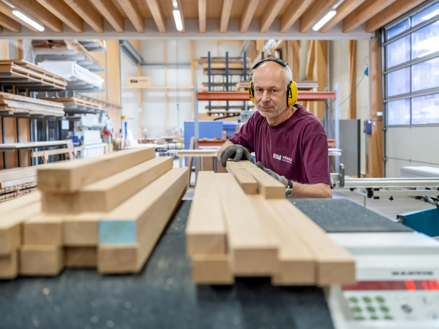 Ein Arbeiter mit Gehörschutz stapelt Holzbalken in einer Schreinerei.