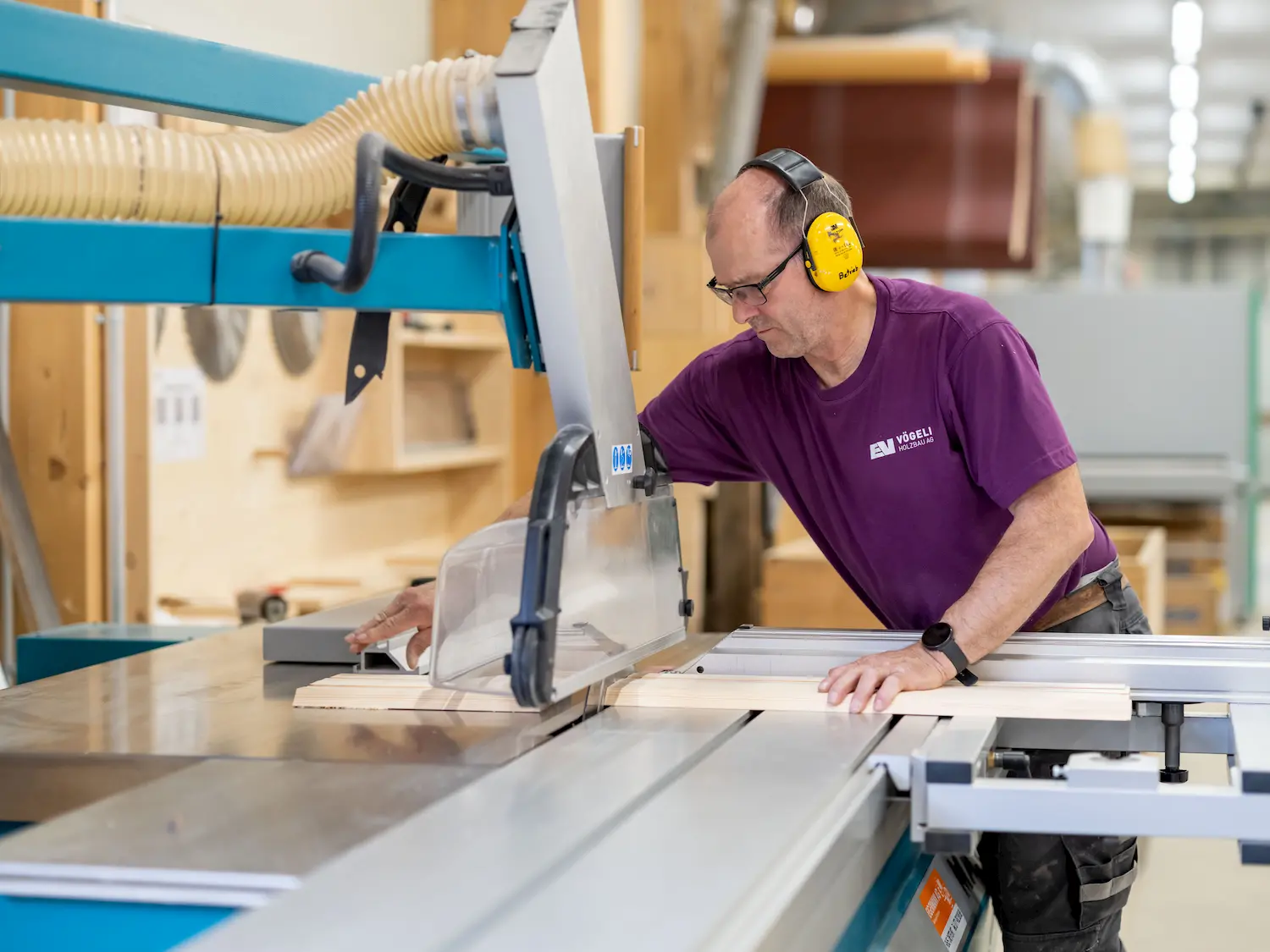 Ein Mann arbeitet konzentriert an einer großen Kreissäge in einer Schreinerei und trägt Gehörschutz.
