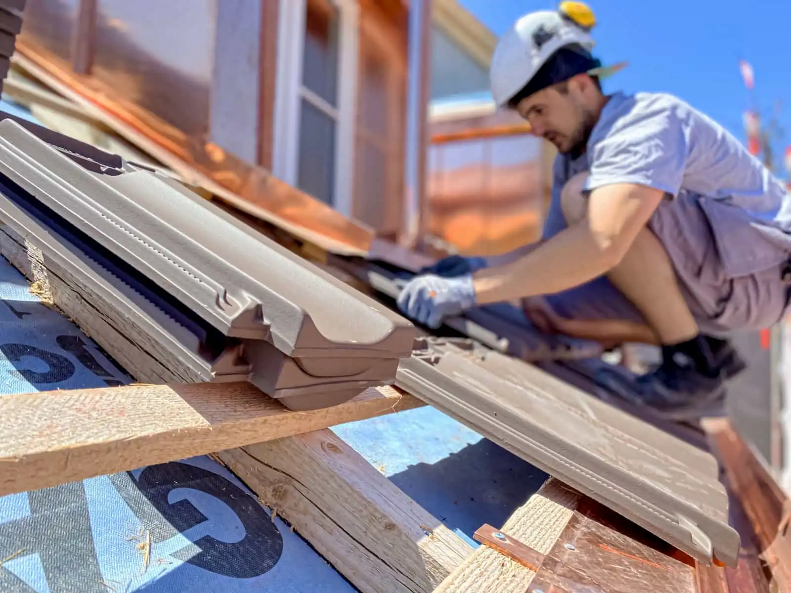 Handwerker bei der Dachsanierung: Arbeiter mit Schutzhelm montiert neue Dachziegel auf einer vorbereiteten Dachkonstruktion.