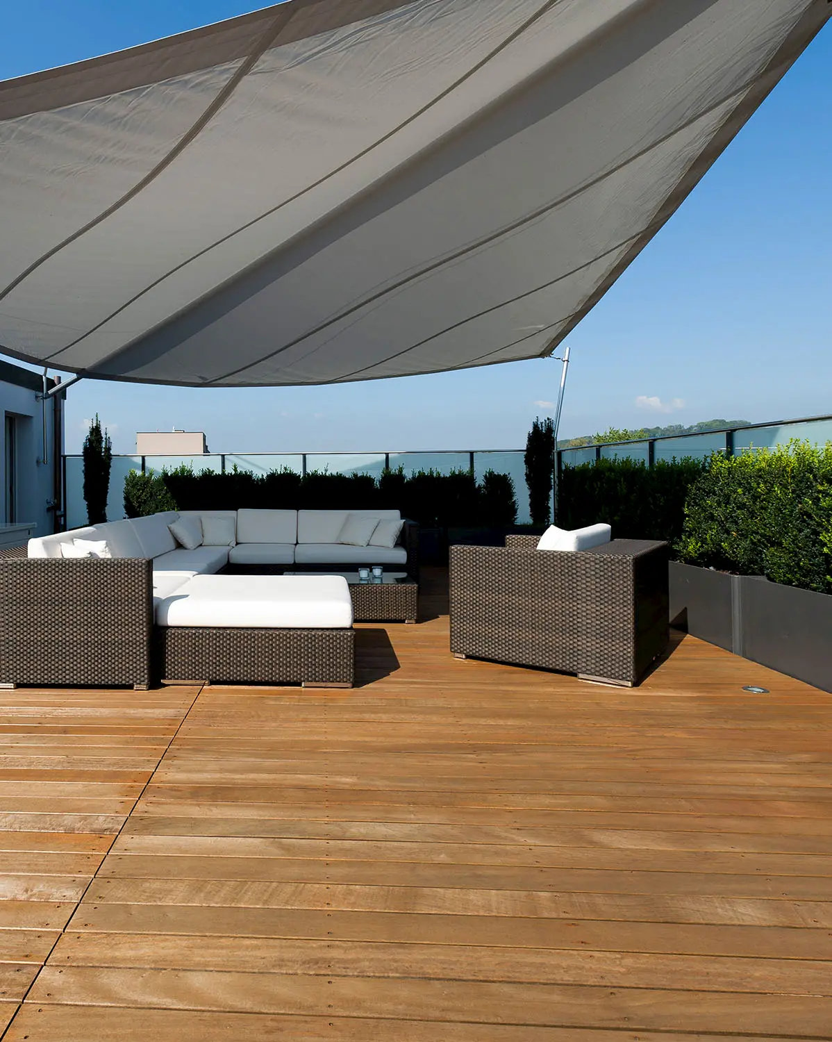 Moderne Terrasse mit Holzrost und Lounge-Möbeln unter Sonnensegel, kombiniert mit Begrünung und Weitblick für ein stilvolles Outdoor-Ambiente.