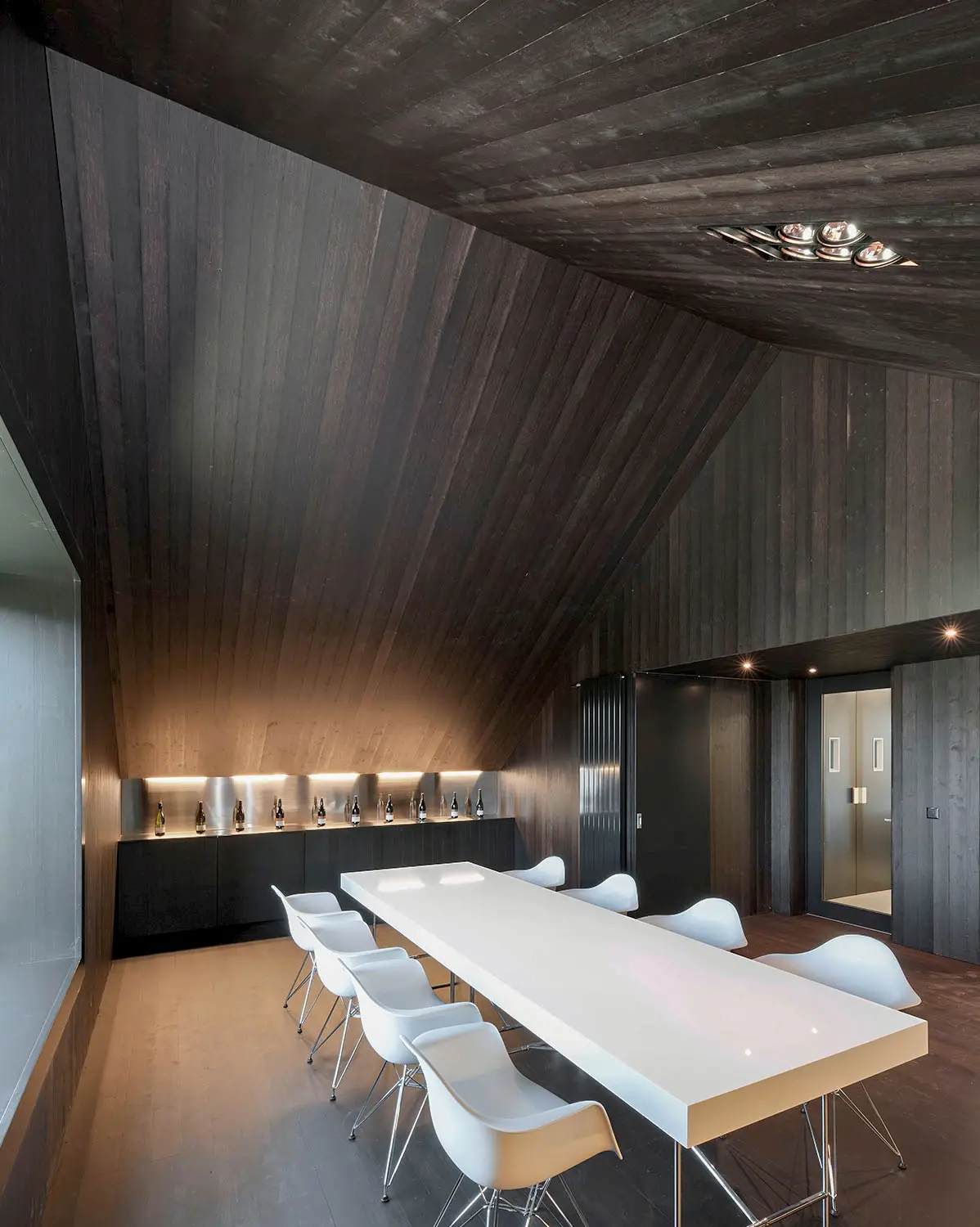 Moderner Innenraum mit dunkler Holzverkleidung, elegantem Esstisch und stimmungsvoller Beleuchtung in minimalistischer Architektur.