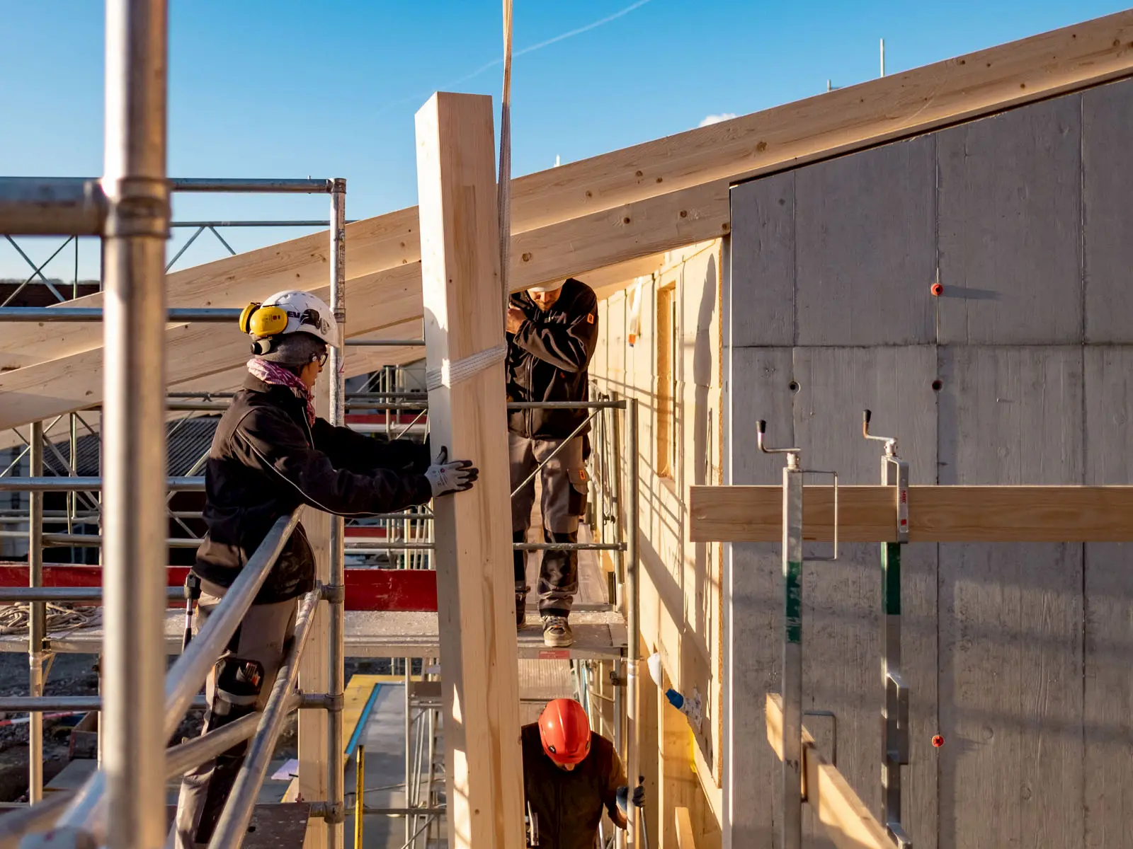 Handwerker montieren massiven Holzpfeiler auf Baustelle, präzise Arbeit im modernen Holzbau bei sonnigem Wetter.