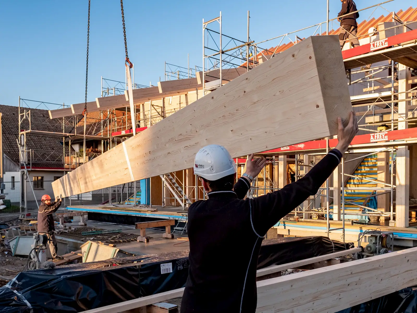 Arbeiter führen Kranmontage eines großen Holzbalkens durch, Koordination und Präzision im modernen Holzbau.