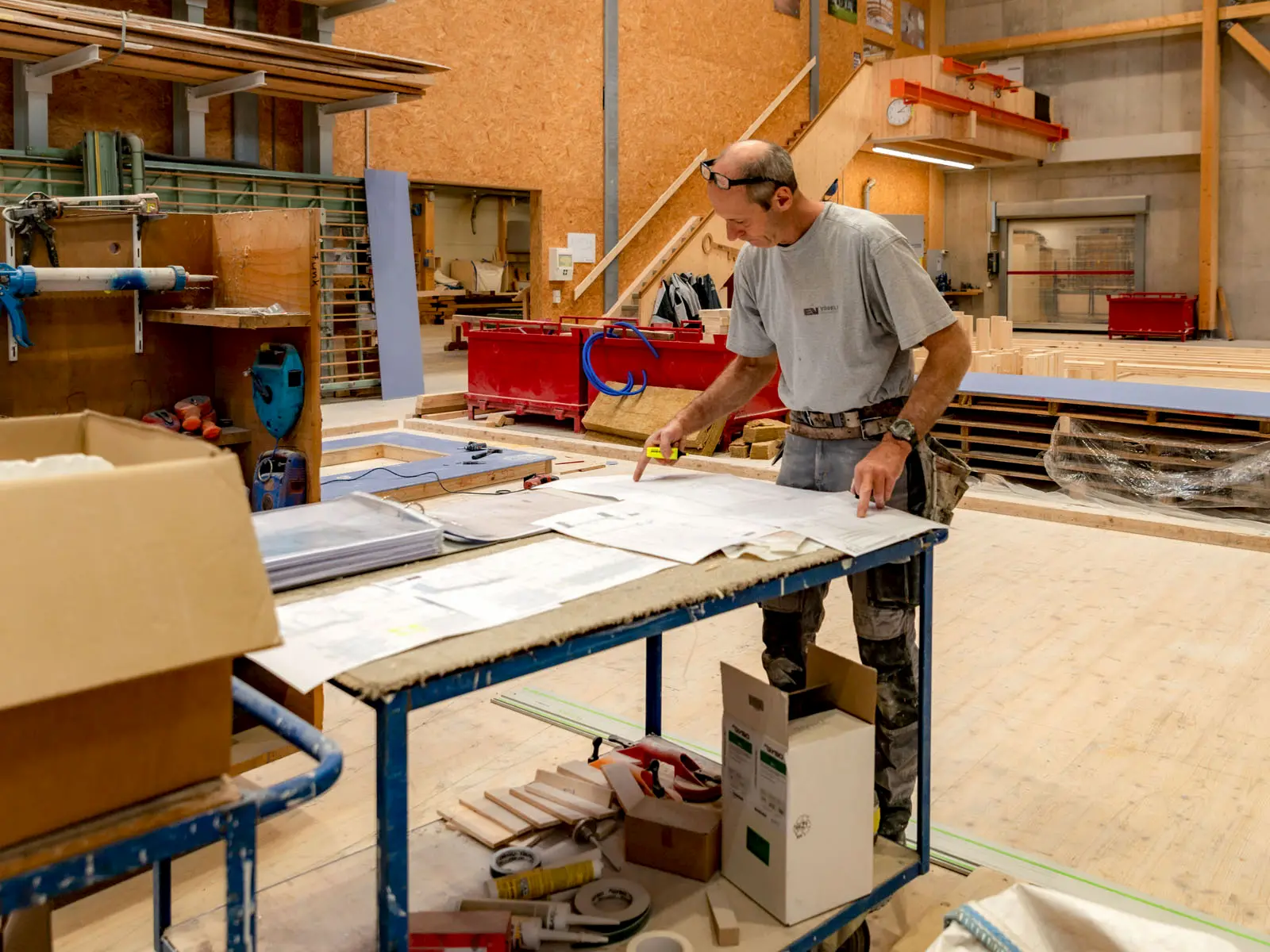 Zimmermann prüft Baupläne in der Werkhalle – exakte Vorbereitung und Qualitätskontrolle bei der Herstellung von Holzelementen.