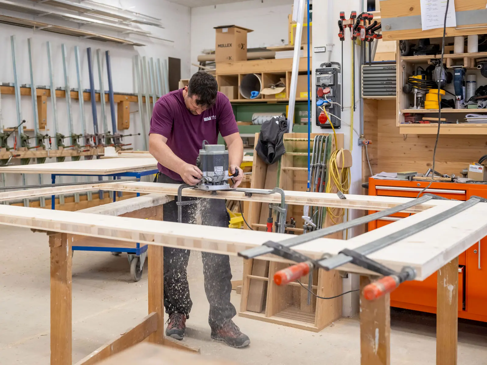 Schreiner fräst Holzrahmen in Werkstatt, sorgfältige Bearbeitung von Massivholz – handwerkliche Präzision und modernes Arbeiten.
