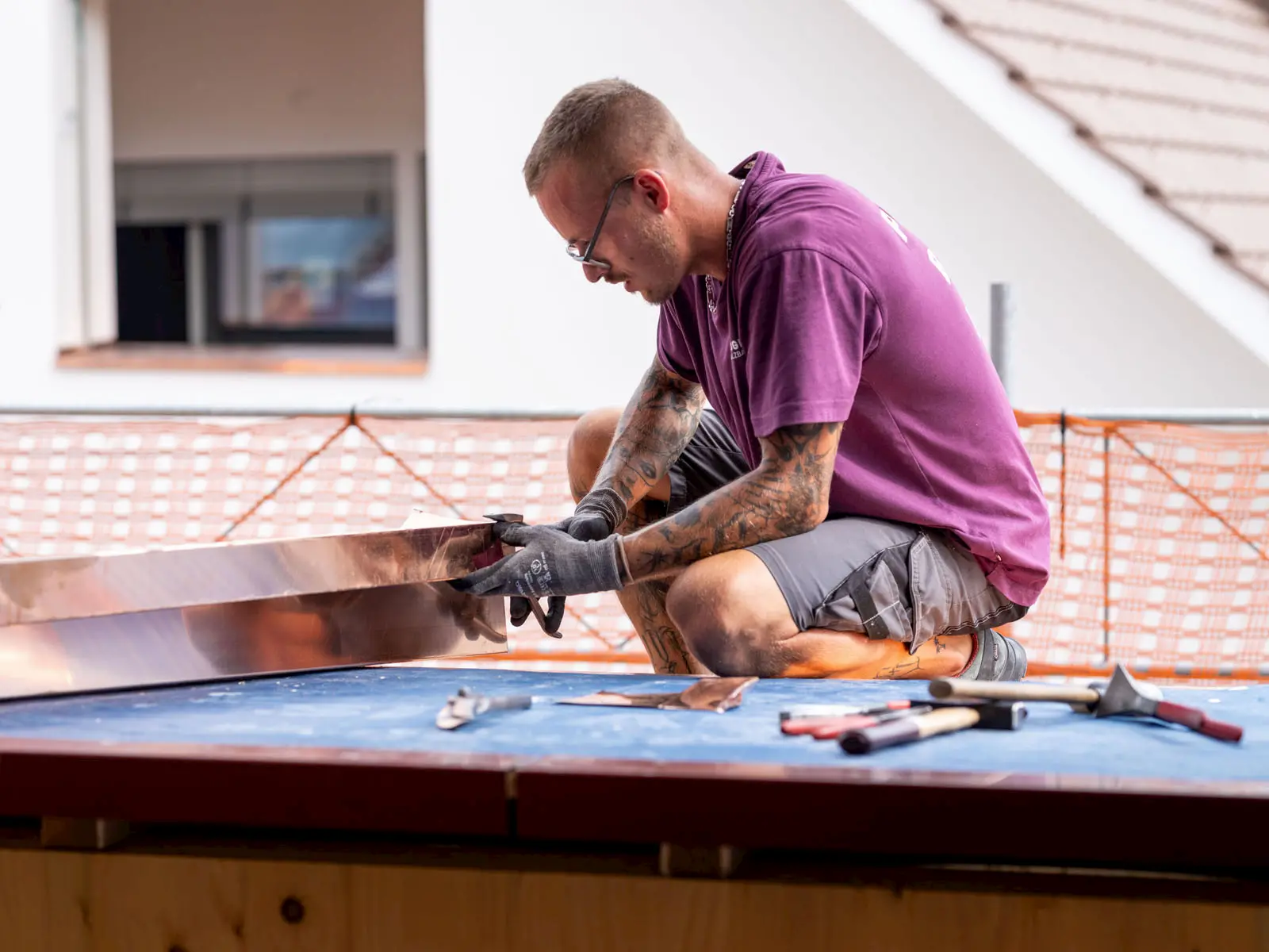 Spengler kniet auf Dach und formt Kupferblech millimetergenau – sorgfältige Verarbeitung und traditionelle Handwerkskunst.