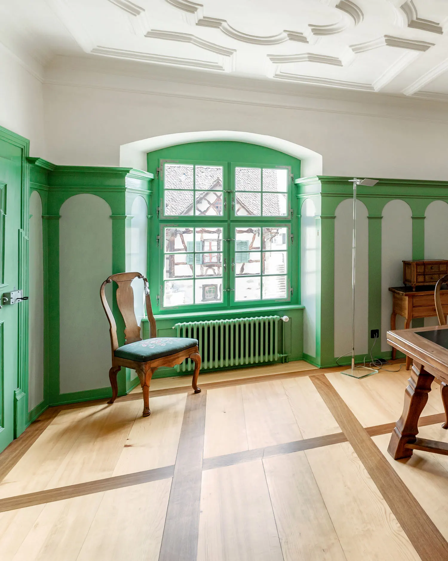 Stilvoll restaurierter Innenraum mit grünem Fensterrahmen, Holzdecke und antiken Möbeln – harmonische Verbindung von Altbau und Handwerkskunst.