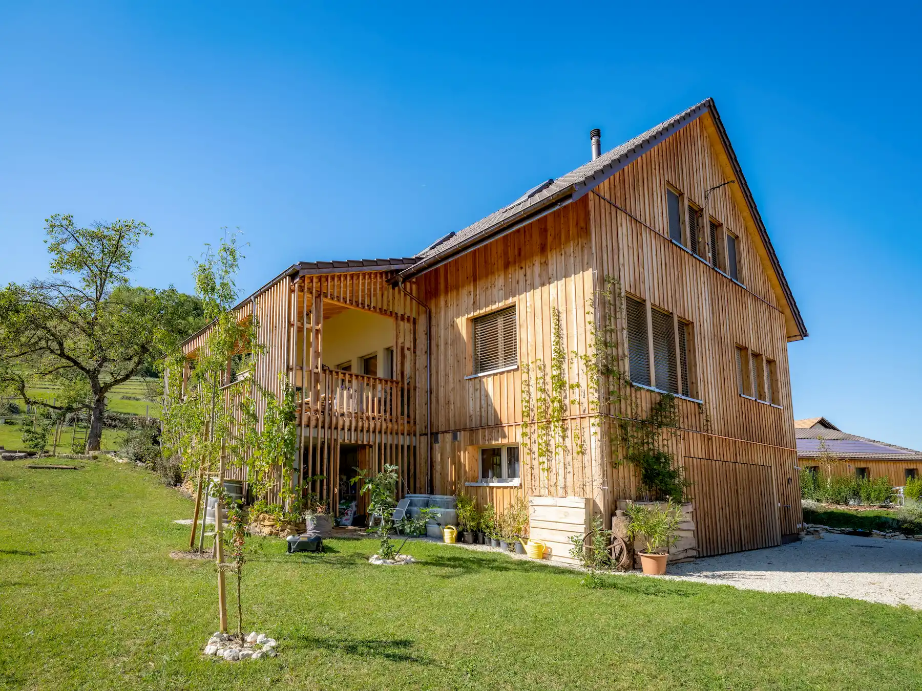 Modernes Einfamilienhaus in Holzbauweise mit vertikaler Lattung – nachhaltige Architektur in natürlicher Umgebung unter strahlend blauem Himmel.