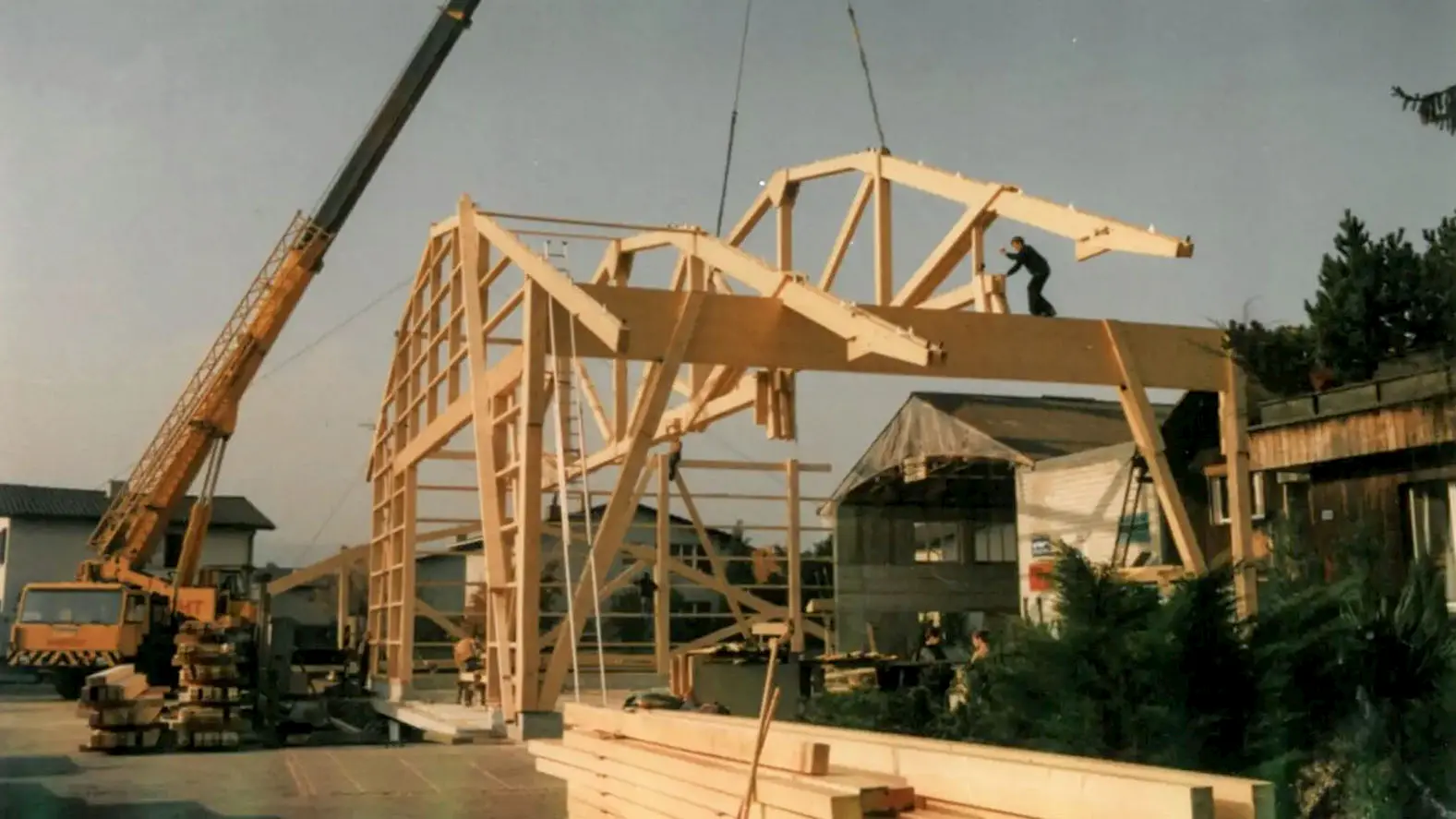 Holztragwerk wird mit einem Kran aufgerichtet, Arbeiter sichern die Holzkonstruktion. Aufnahme 1986