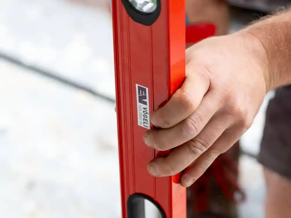 Hand hält eine rote Wasserwaage mit dem Aufkleber EV Vögele Holzbau AG.