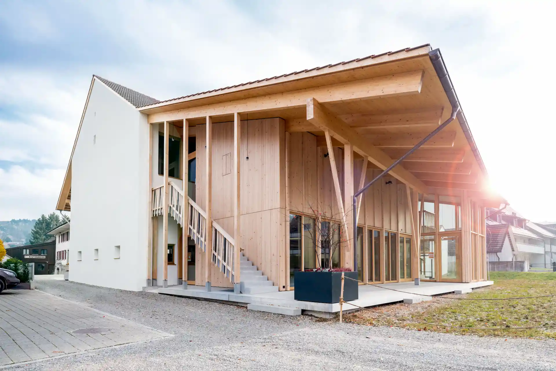 Modernes Haus mit Fassade in Holzoptik und offenen Außentreppen, hellem Himmel im Hintergrund.