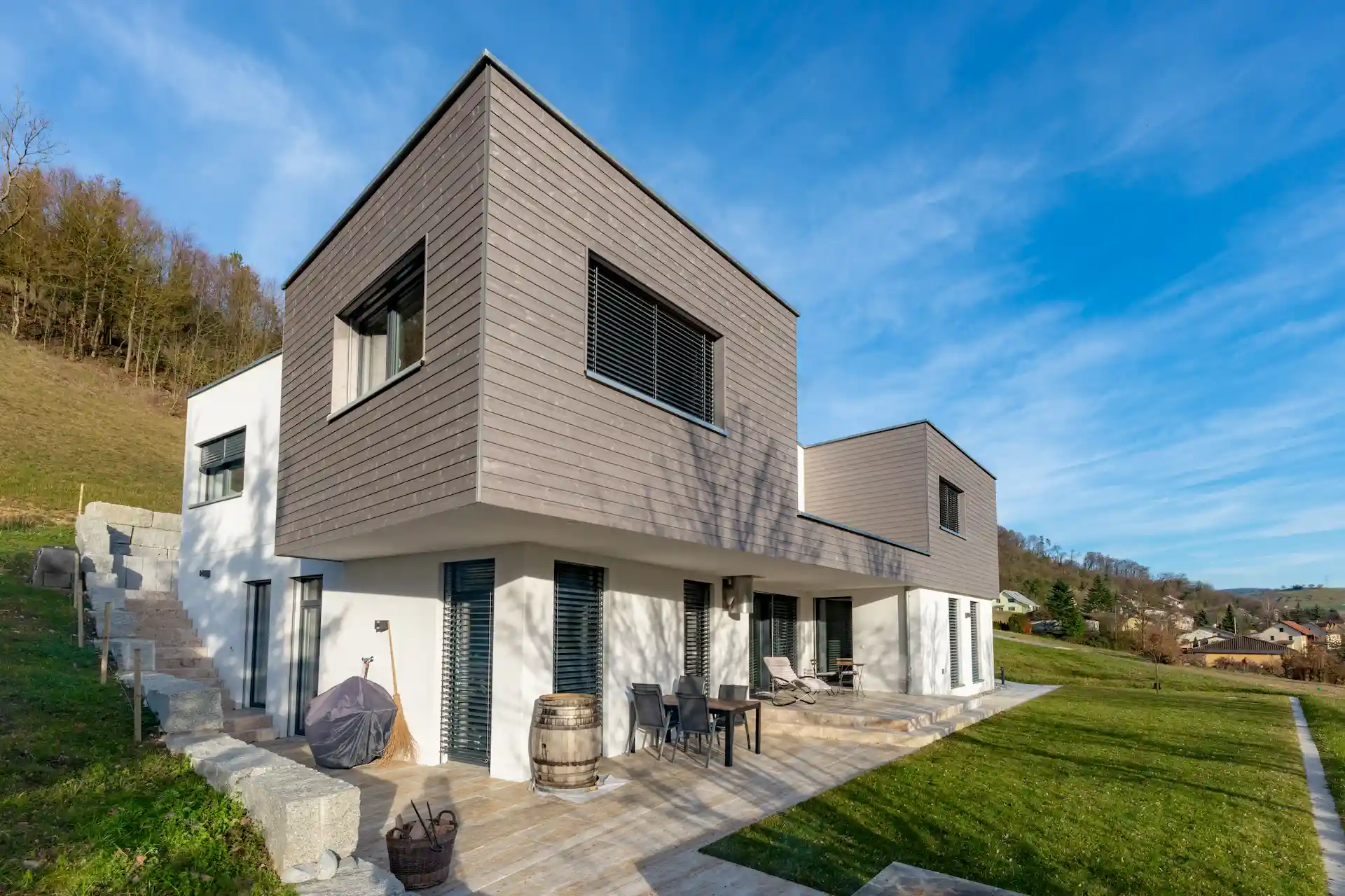 Modernes zweistöckiges Haus mit Holzverkleidung im Obergeschoss und Terrasse unter blauem Himmel.