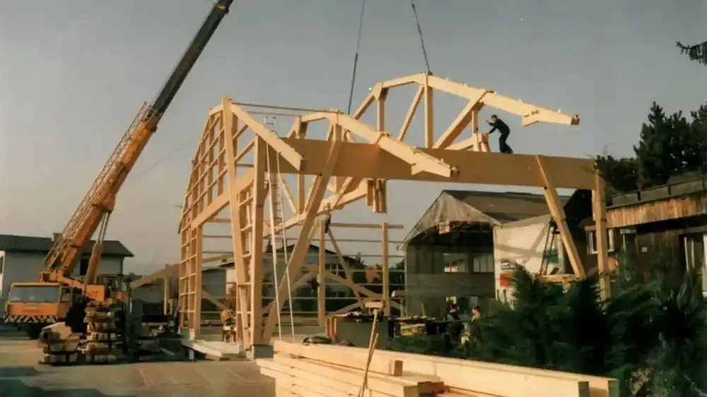 Auf dem Bild sind mehrere Holzbinder und ein Kran zusehen. Das Bild entstand 1986 bei den Erweiterungsmassnahmen der Vögeli Holzbau