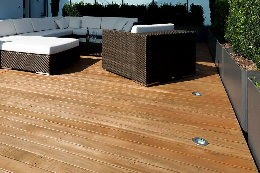 Moderne Terrasse mit Holzboden, integriertem Bodeneinbauspot und Polyrattan-Lounge mit weißen Kissen.
