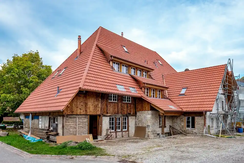 Historisches Bauernhaus mit neuem roten Ziegeldach und Gerüst an der rechten Seite.