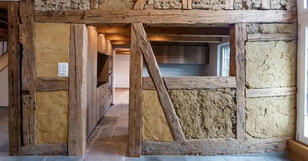 Historische Fachwerkwand mit Lehmfüllung und Blick in eine moderne Küche mit Holzfronten.