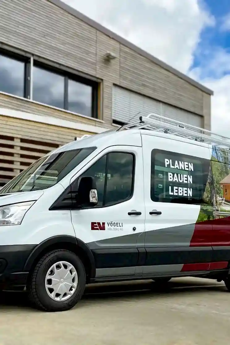 Weisser Service-Van mit der Aufschrift 'PLANEN BAUEN LEBEN' vor modernem Gebäude.