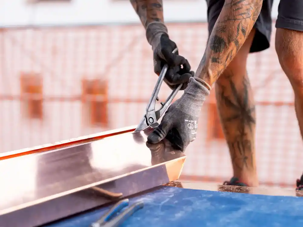 Tattooierter Arbeiter schneidet Metallblech mit Blechschere auf einer Baustelle.