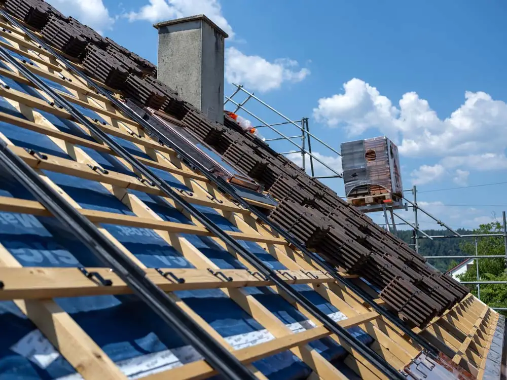 Dach unter Dachziegel-Neuverlegung mit Dachlatten, Dachziegeln und Kamin bei sonnigem Wetter.