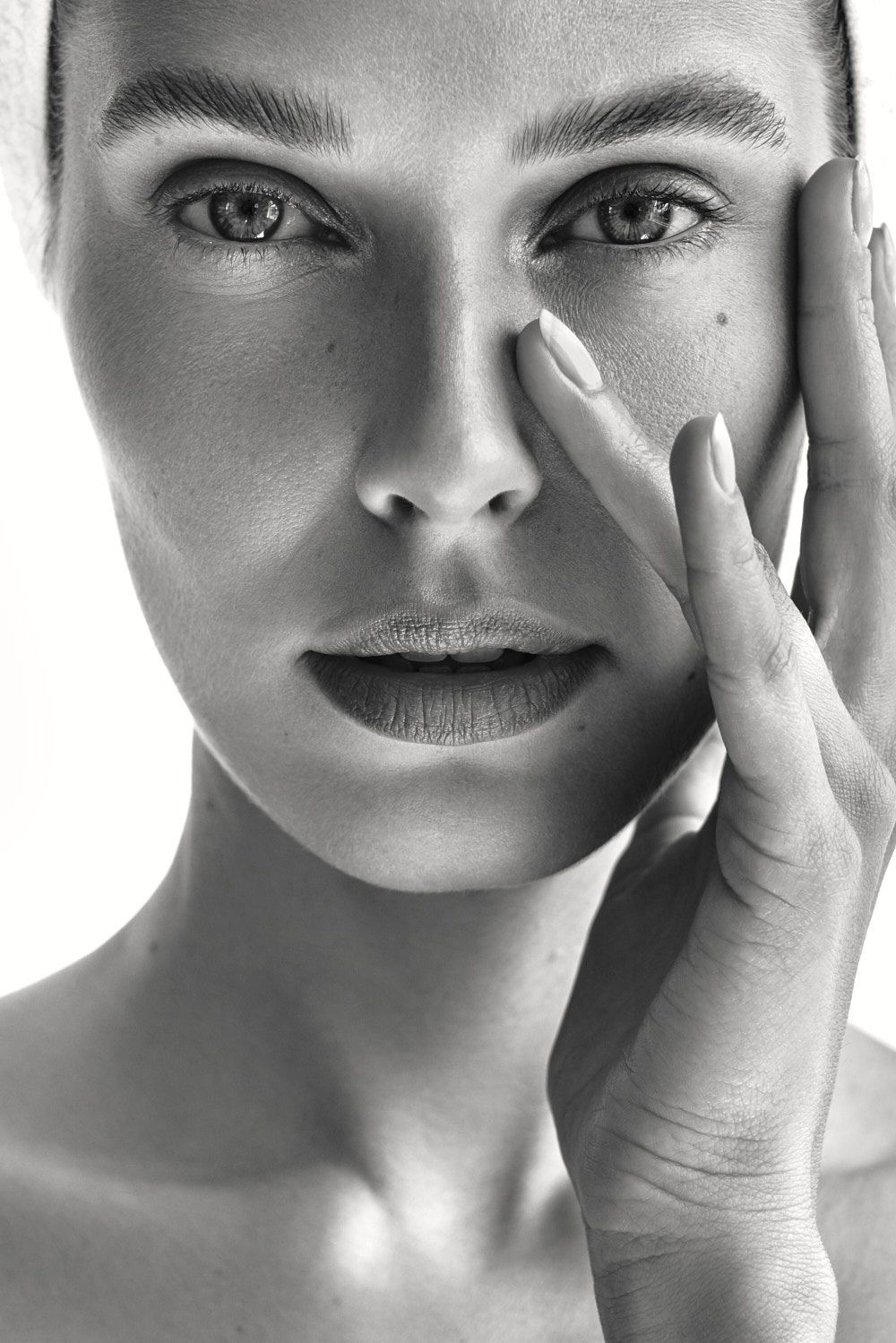 Melna un balta tuvplāna sievietes seja ar roku pie vaiga un skaidrām acīm.