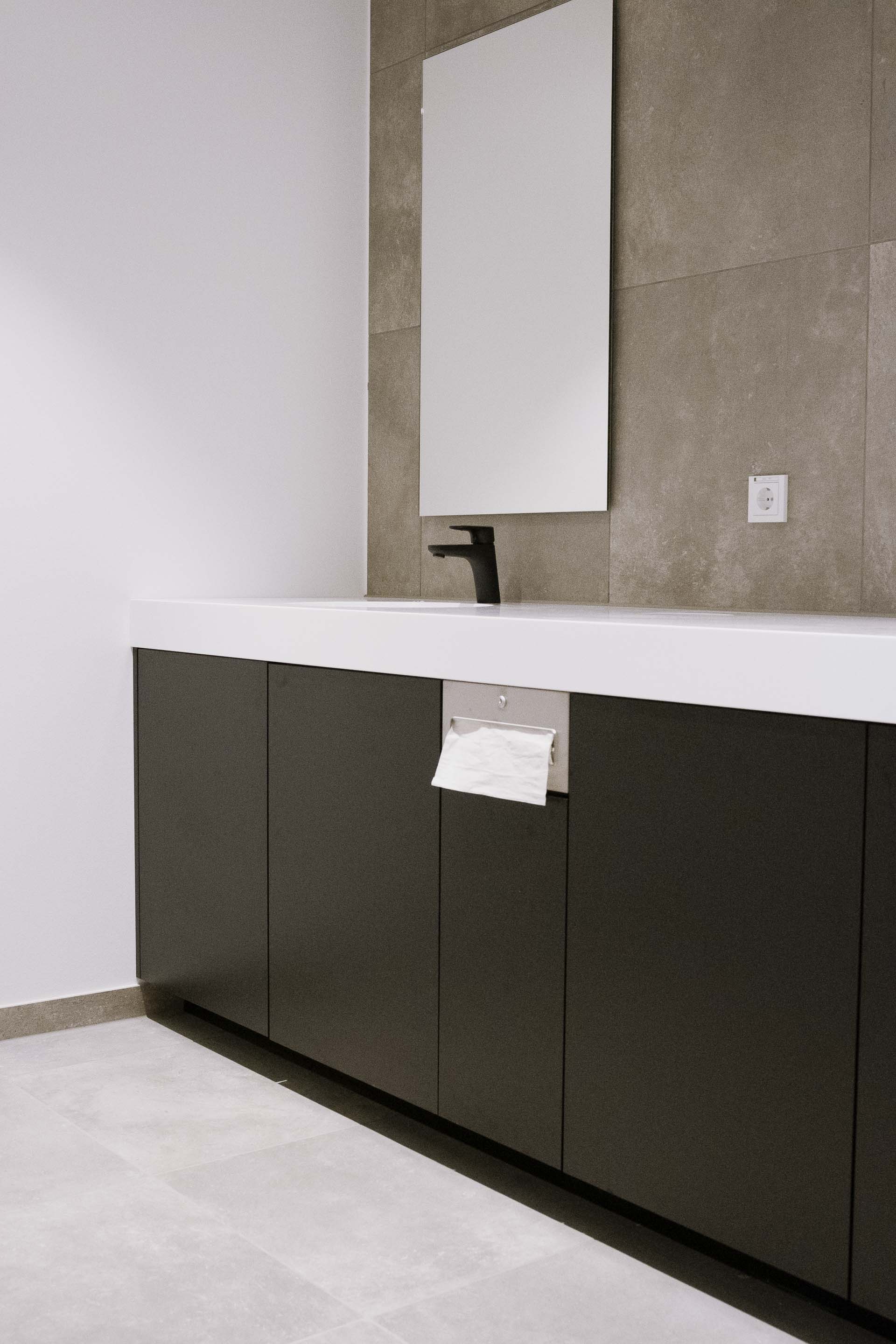Modern bathroom vanity with matte black cabinets, white countertop, black faucet, rectangular mirror, and built-in tissue dispenser.
