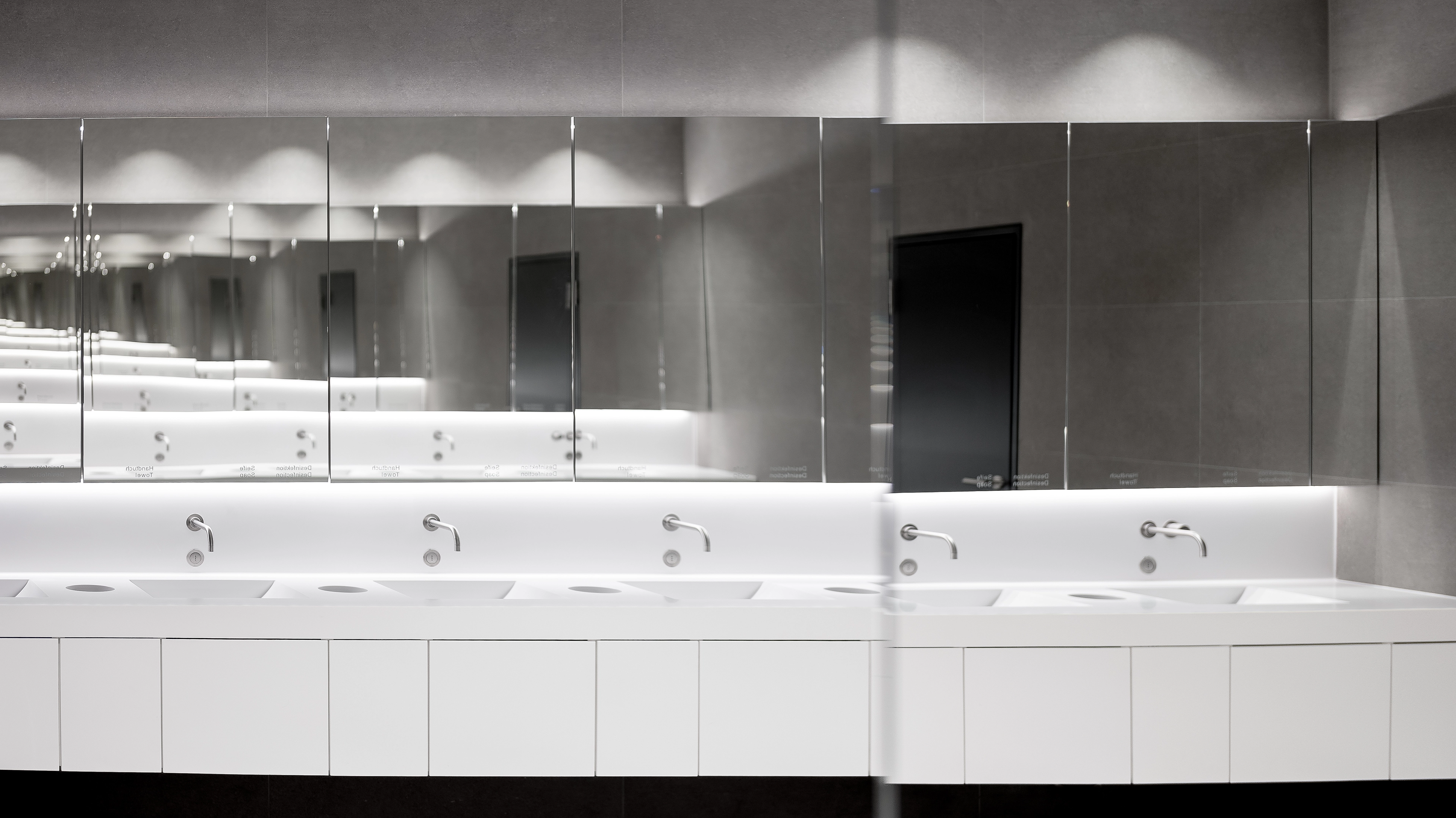 Modern public restroom sinks with wall-mounted faucets and large mirrors reflecting the space.