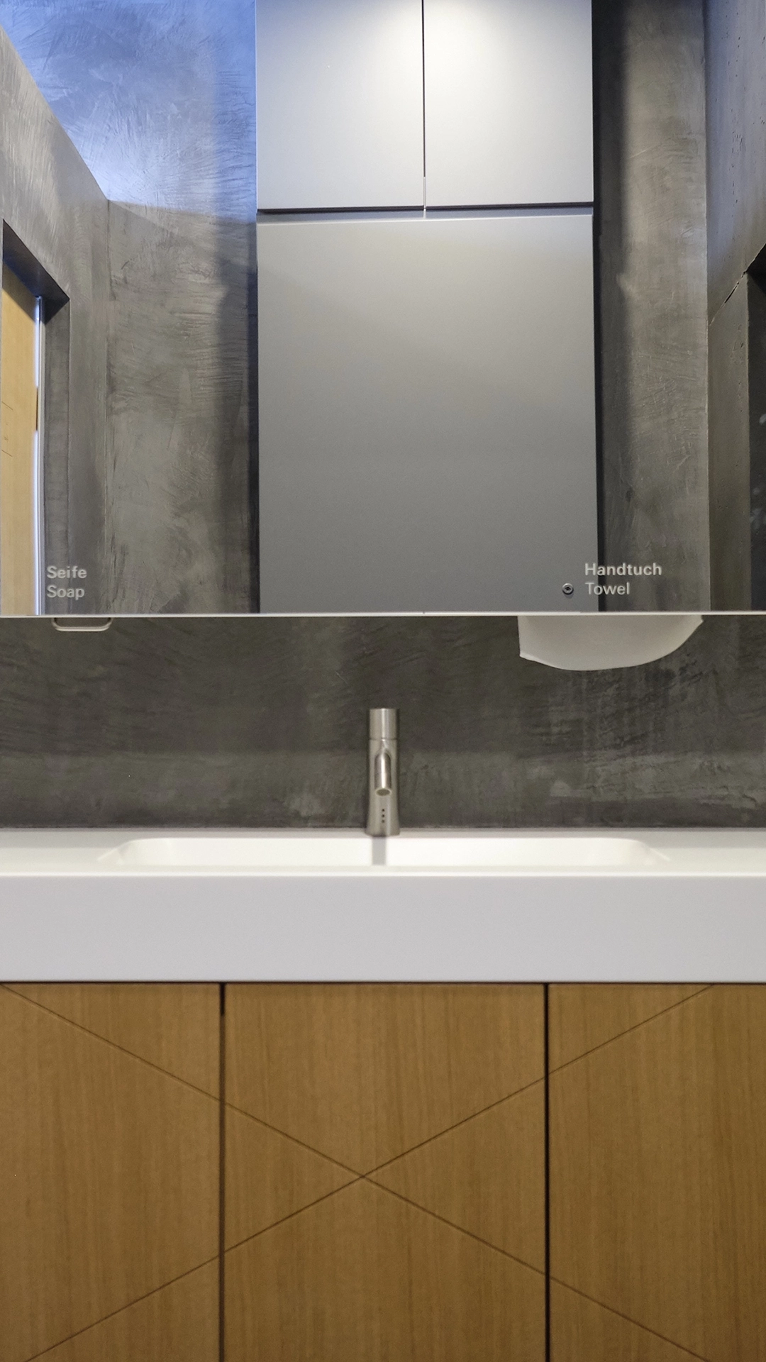 Modern bathroom sink with a stainless steel faucet, a large mirror, and wooden cabinet below.