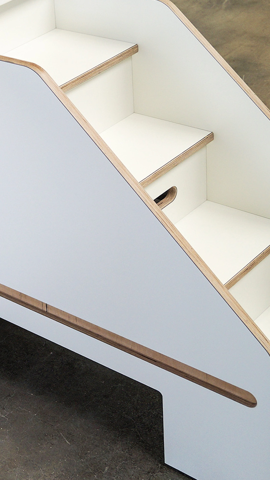 Close-up of a modern, white wooden staircase with visible layered edges and a cut-out handle on the side panel.