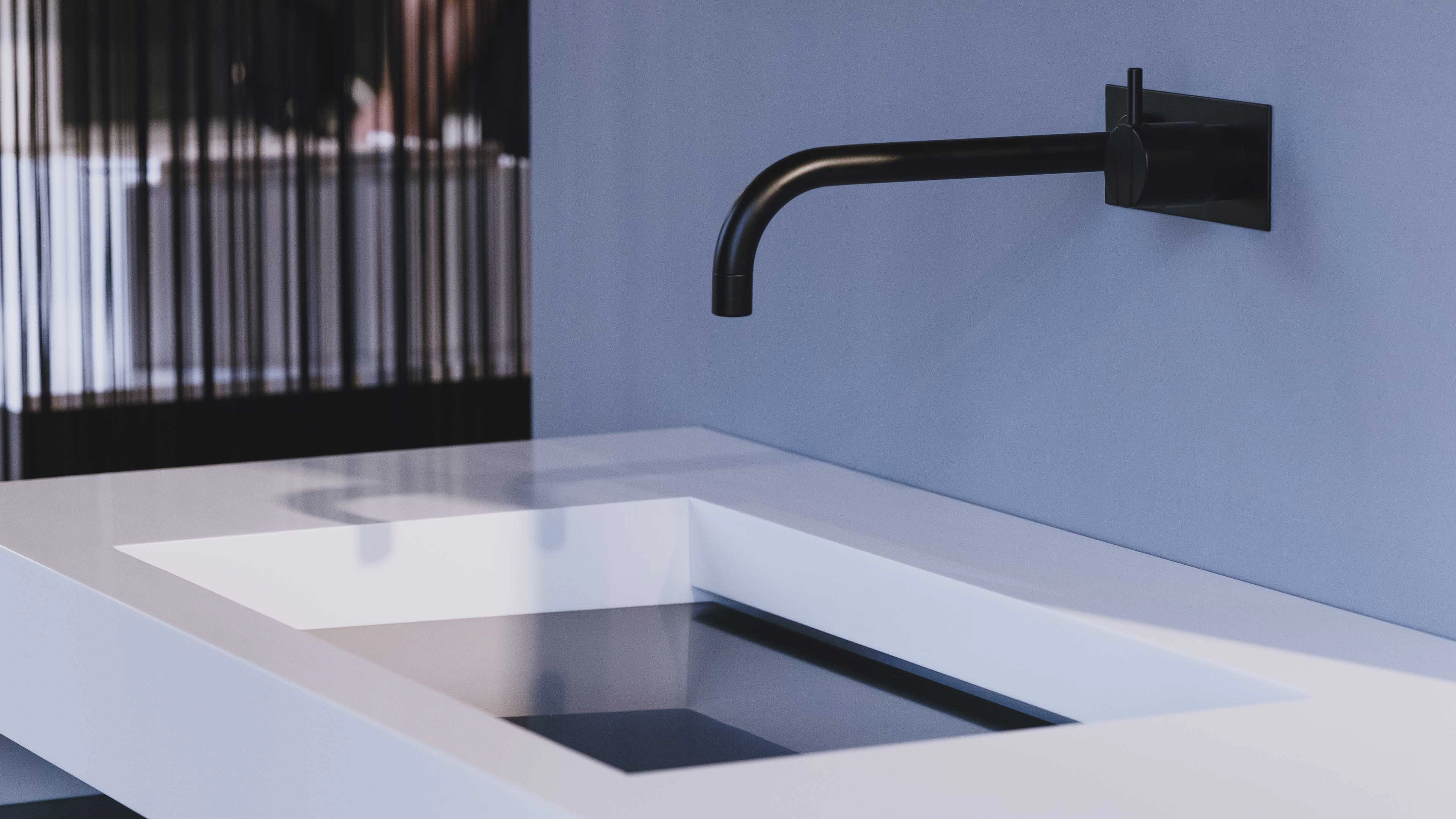 Modern white rectangular sink with a black wall-mounted faucet and blue wall background.