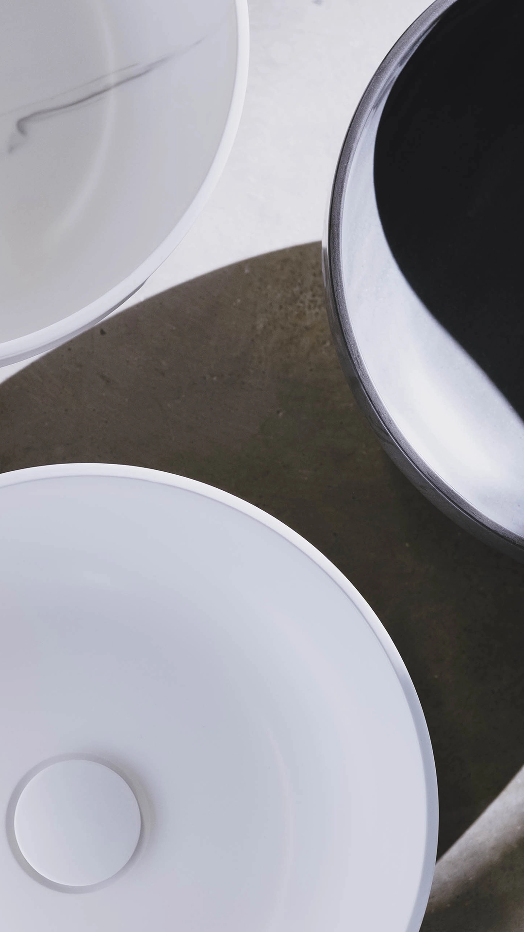 Top view of three round bowls with smooth surfaces in white and black, casting soft shadows on a light background.