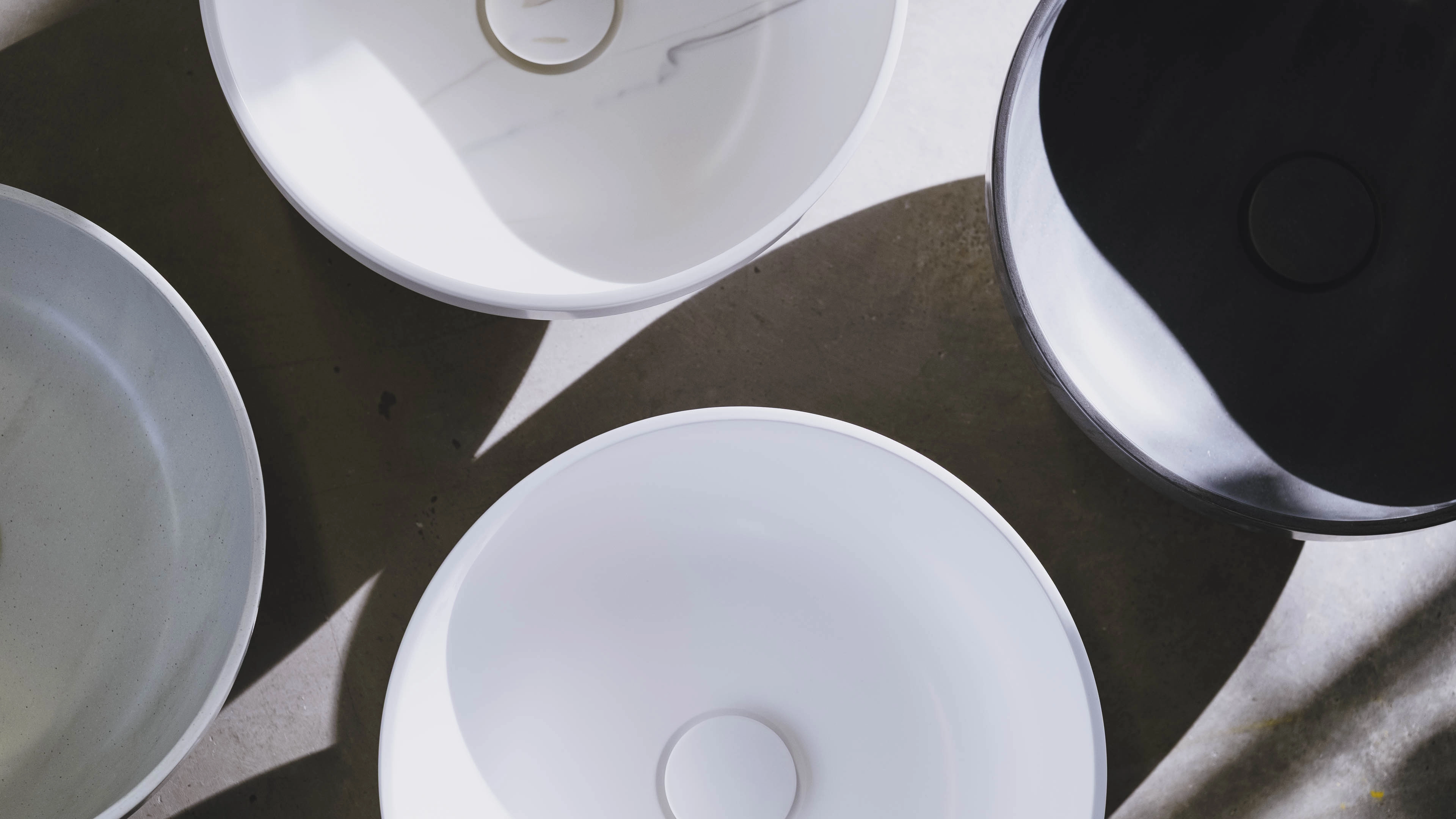 Top view of four empty ceramic bowls in white, gray, and black colors casting shadows on a concrete surface.