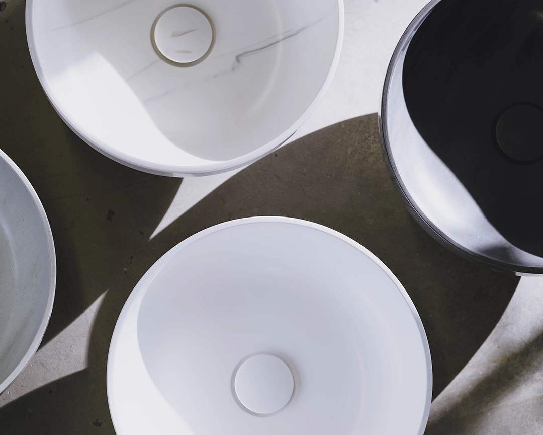Top view of four round vessel sinks in white, black, and gray, arranged on a gray surface with shadows.