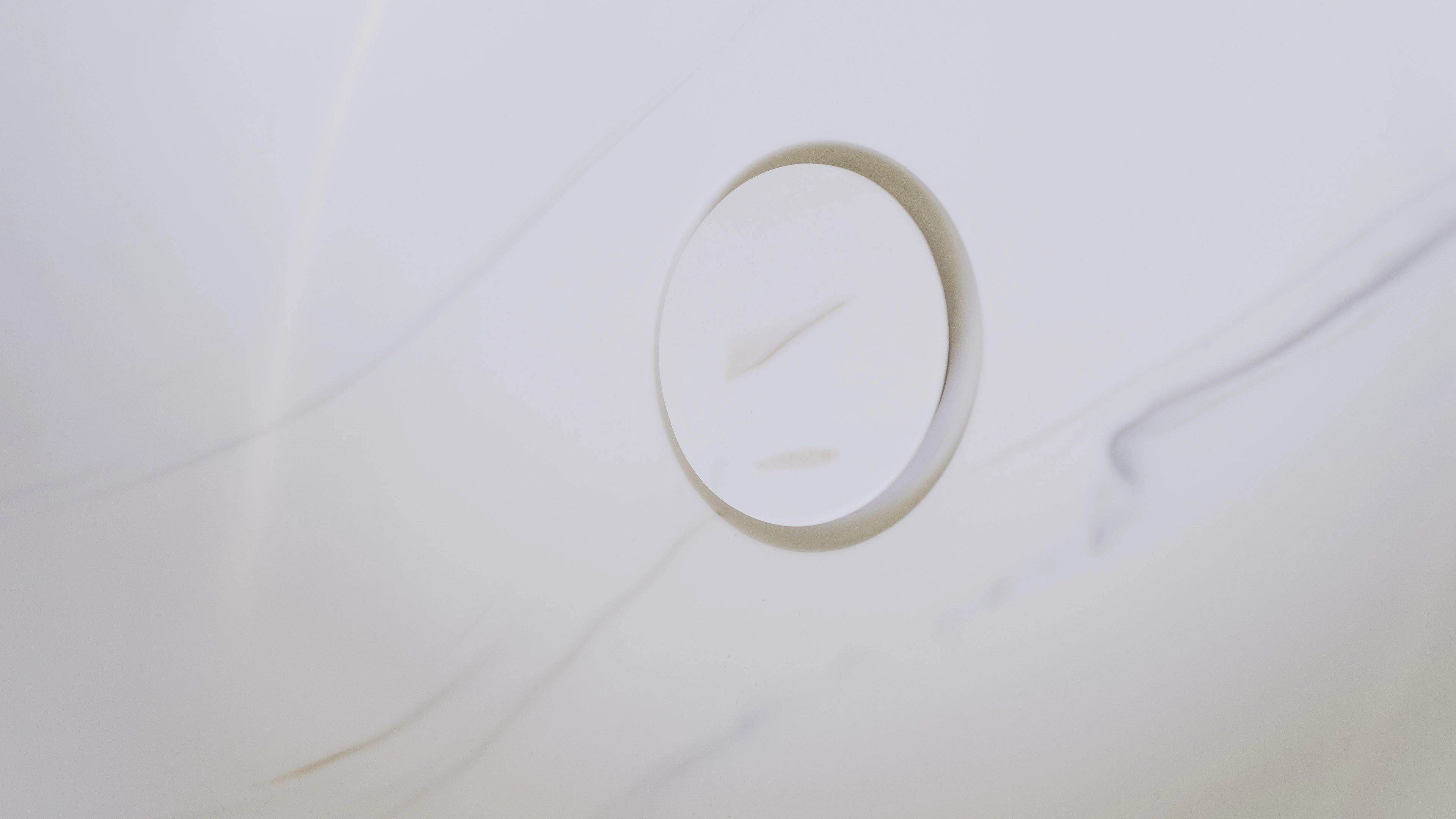 Close-up of a white circular drain cover on a white marble surface with subtle grey veins.