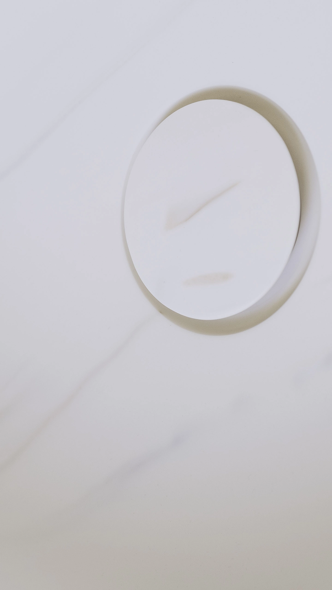 Close-up of a minimalist white circular sink drain cover on a light marble surface.