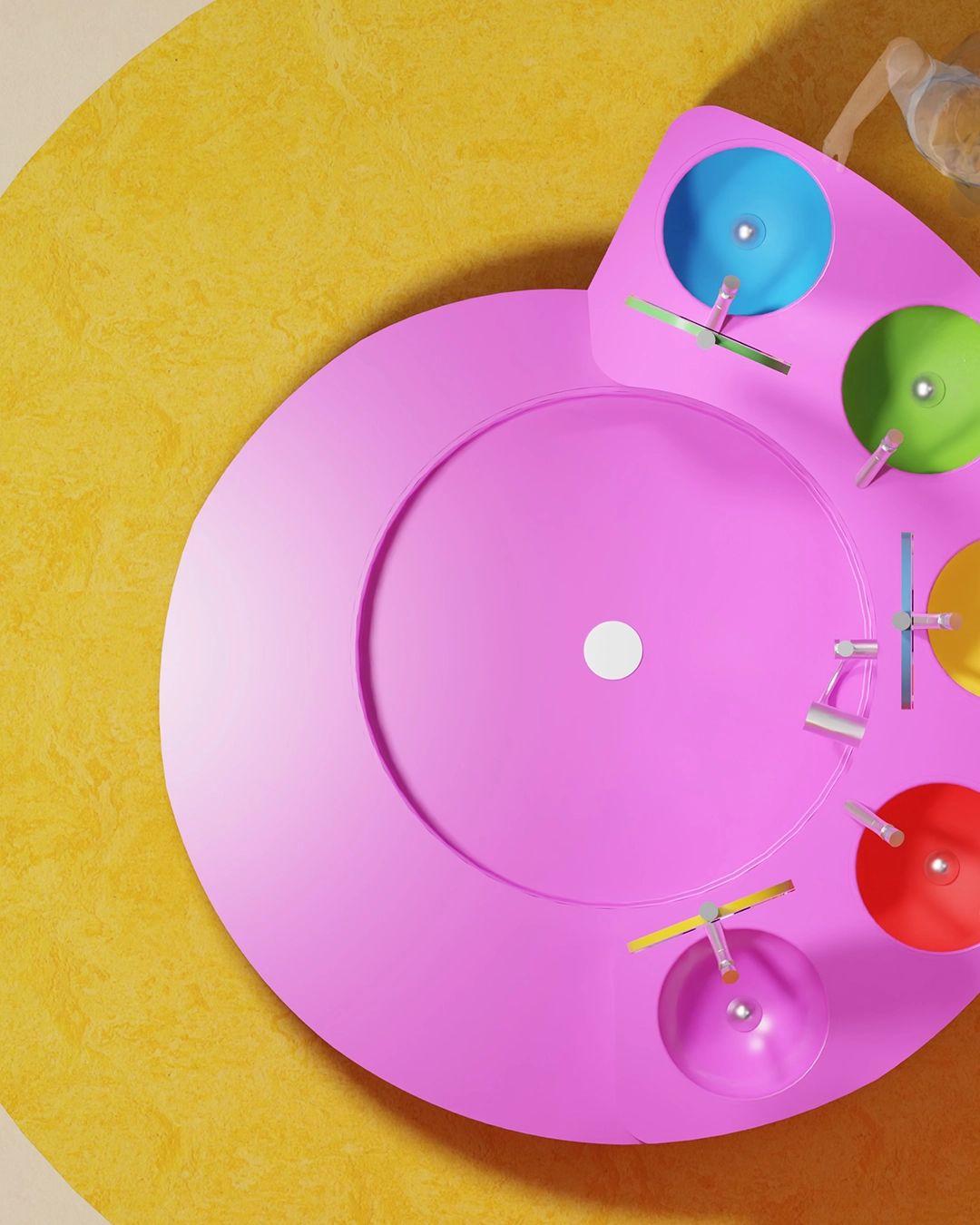 Top view of a round pink sink with five colorful smaller basins in blue, green, yellow, red, and purple arranged on a yellow textured floor.