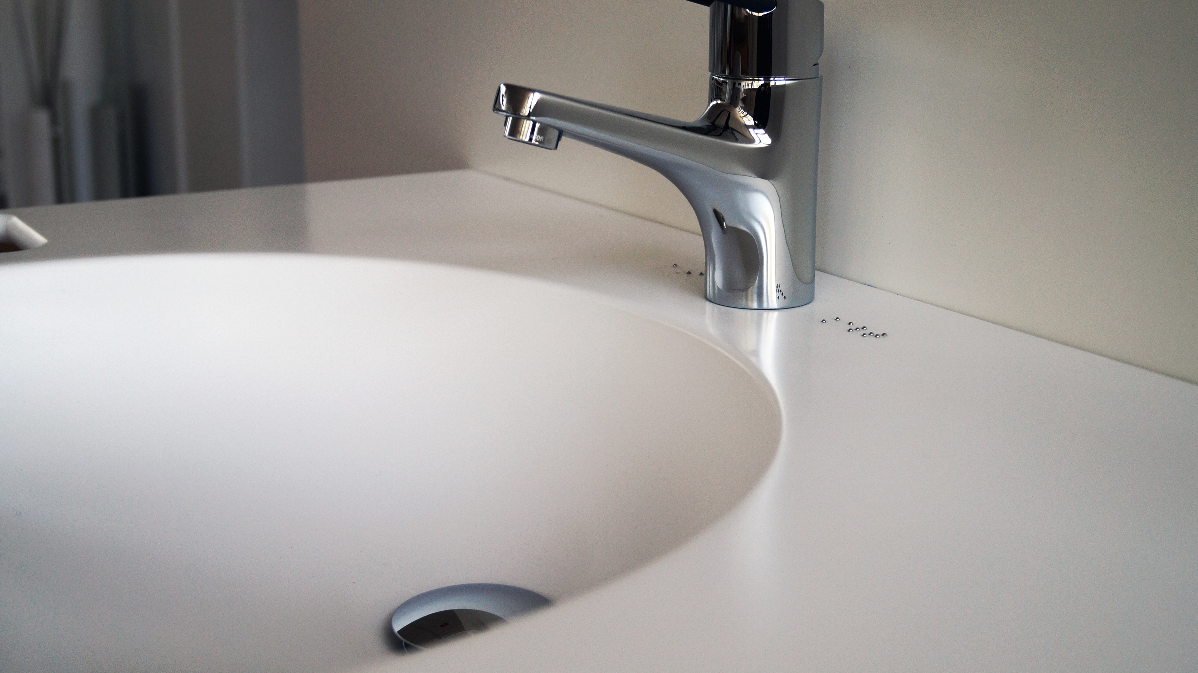 Close-up of a modern chrome faucet mounted on a white sink with a beige background.