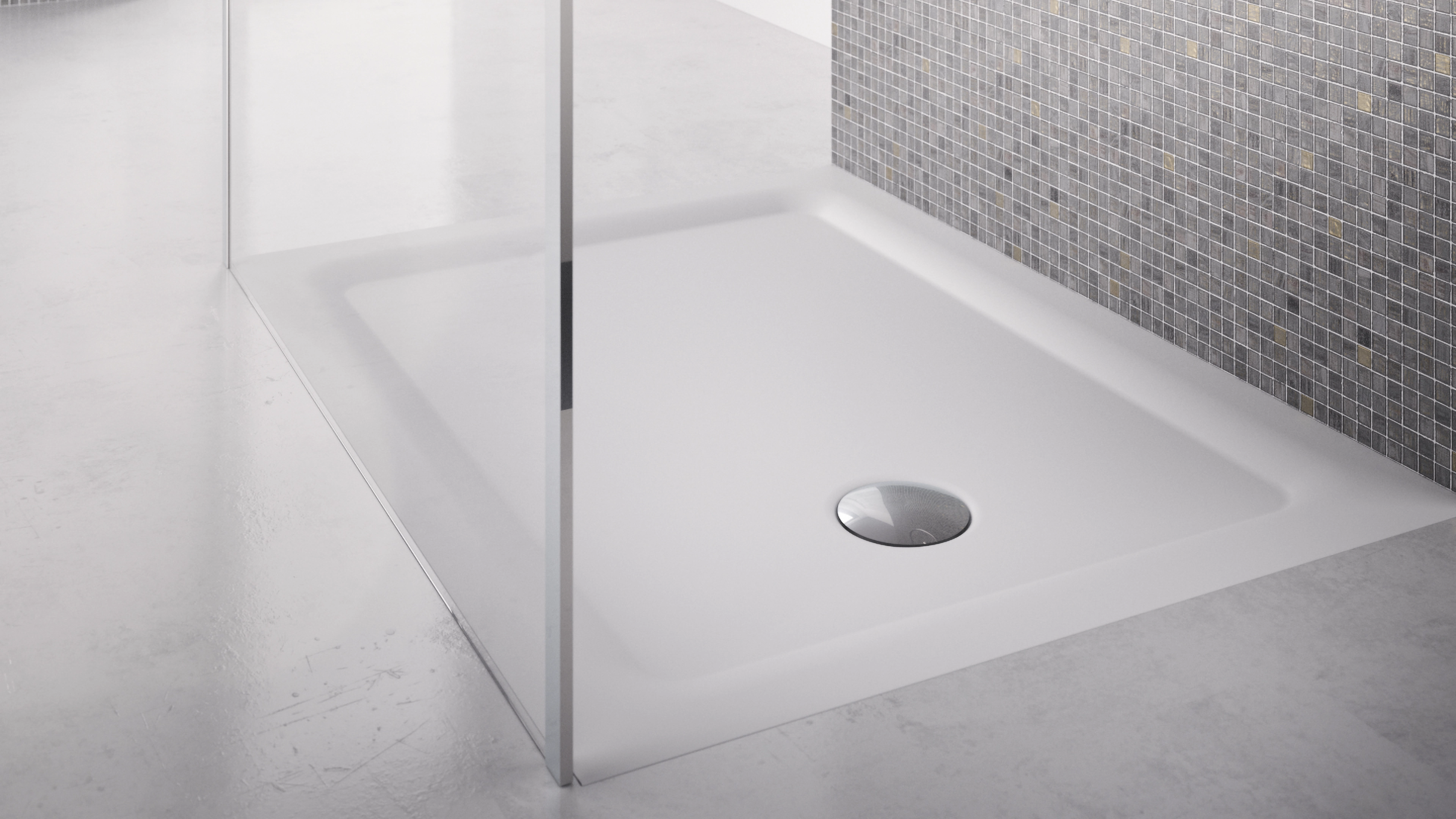 White rectangular shower base with a central drain, next to a tiled wall and glass shower partition.