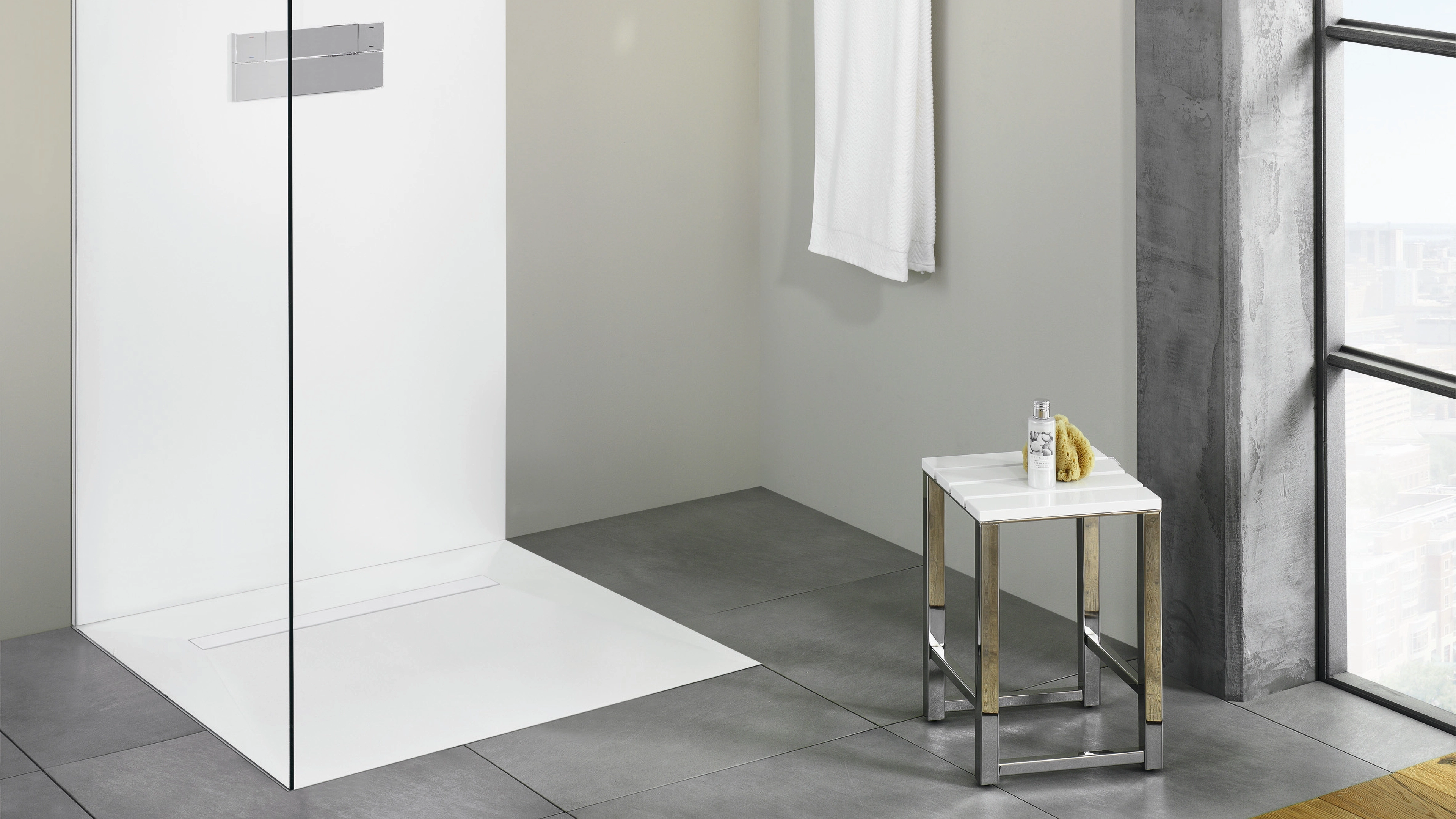 Minimalist walk-in shower with glass partition, gray tiles, and a small stool holding a bottle and yellow sponge.