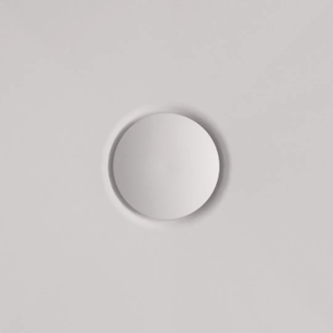 Minimalist round recessed button or dial on a smooth light gray surface.