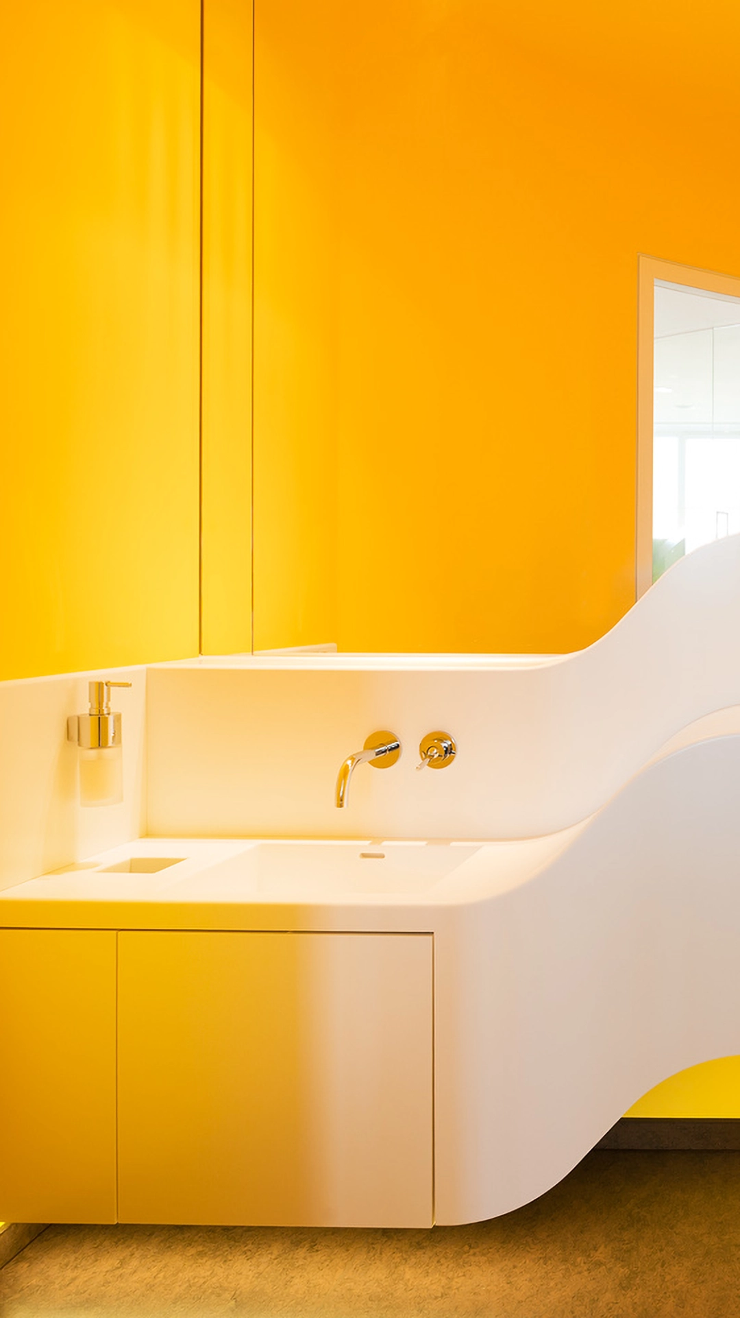 Modern white bathroom sink with a curvy design and wall-mounted faucet against a bright yellow wall.