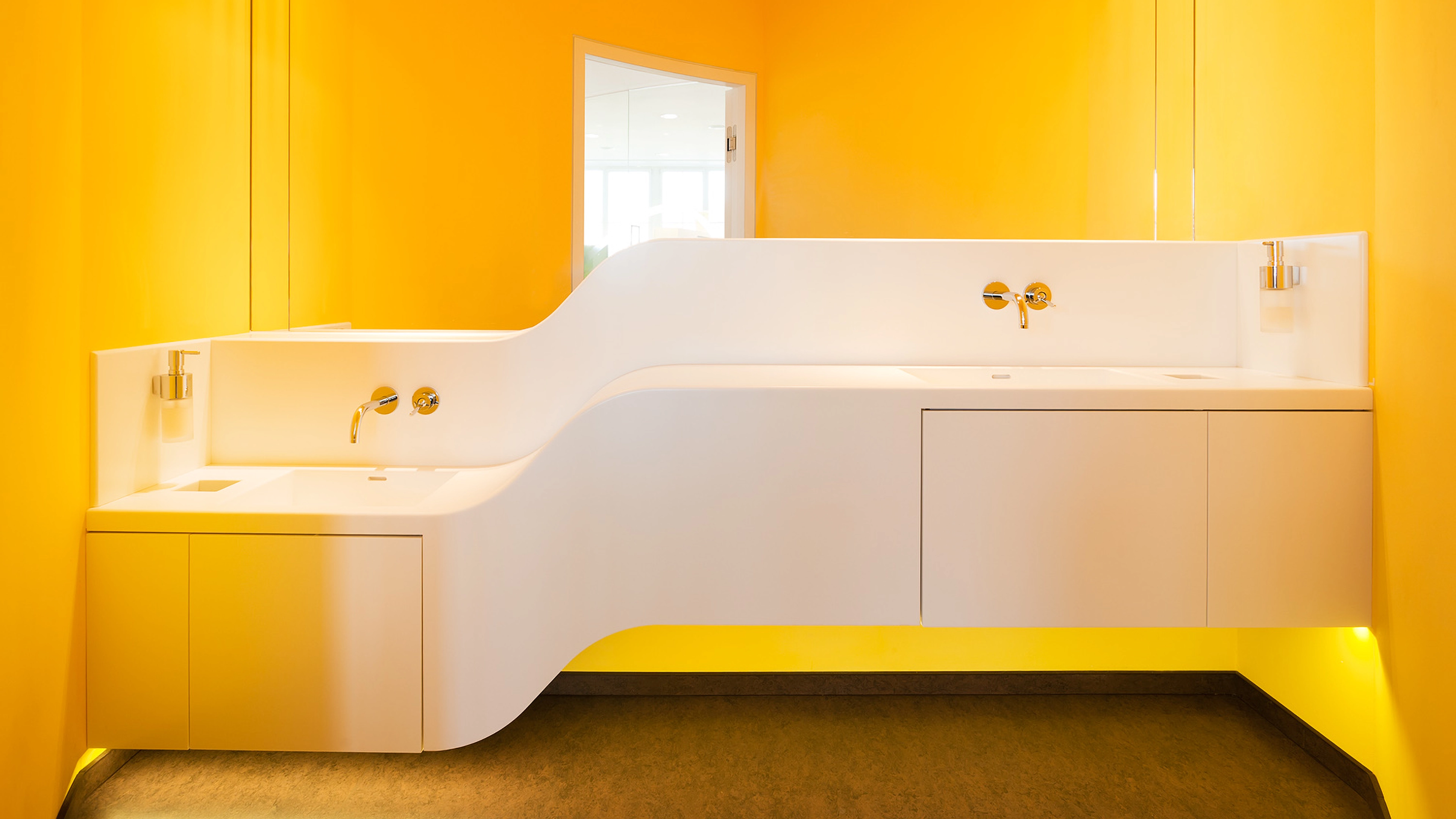 Modern white double sink with curved design mounted on bright yellow bathroom walls.