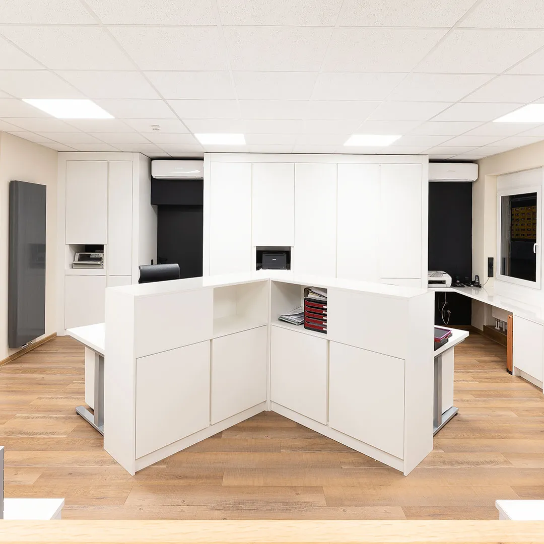 Modern office reception desk with white cabinetry, wooden flooring, and black office chairs.