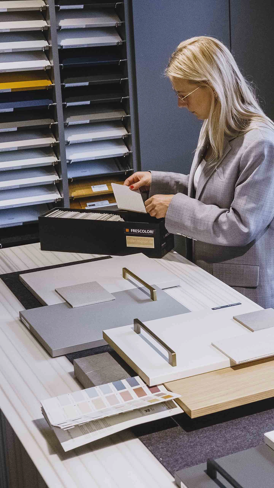 Woman examining color and material samples on a table with cabinet handle displays and color swatches in a showroom.