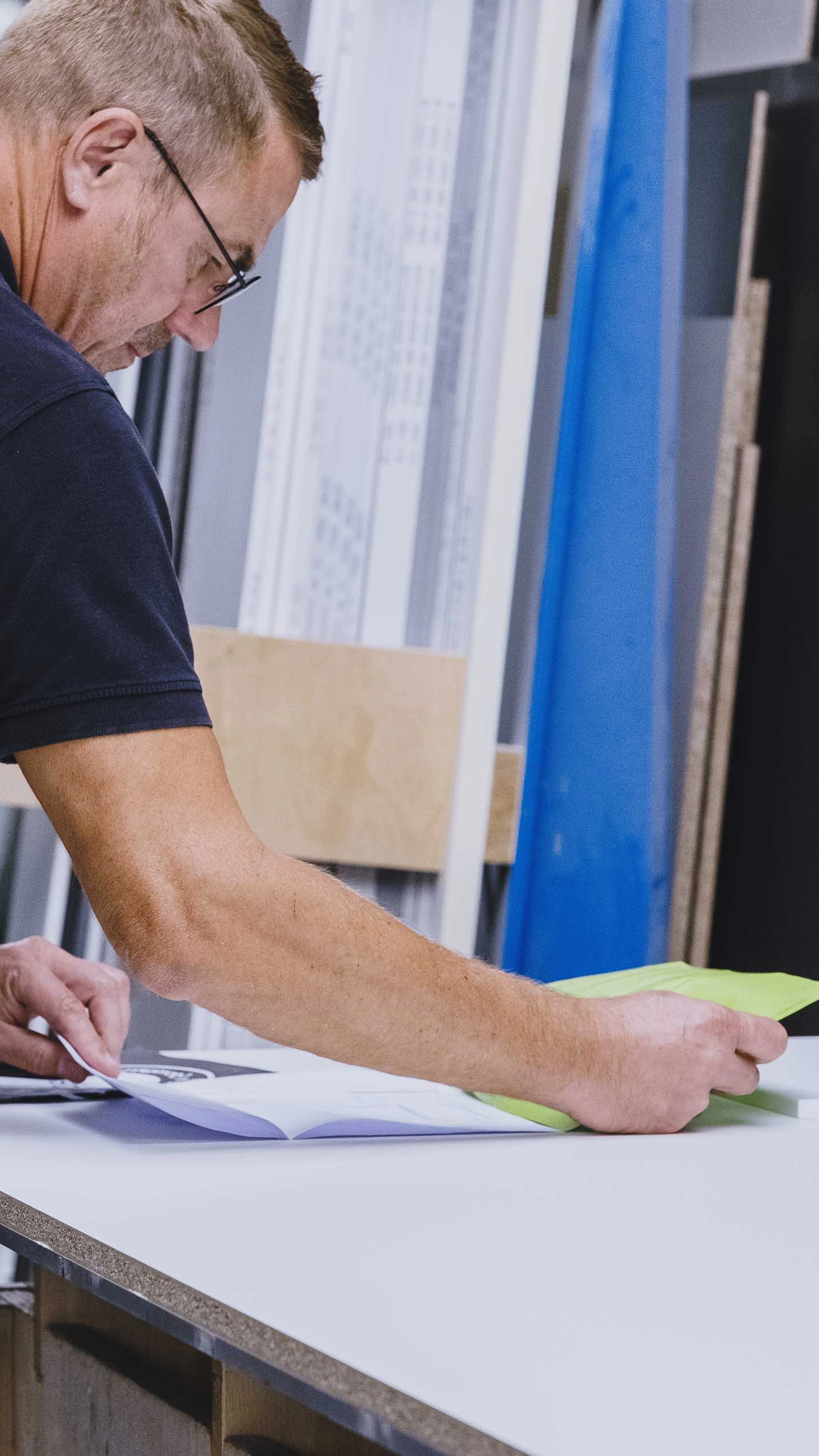 Man examining documents on a white table in a workshop or office setting.