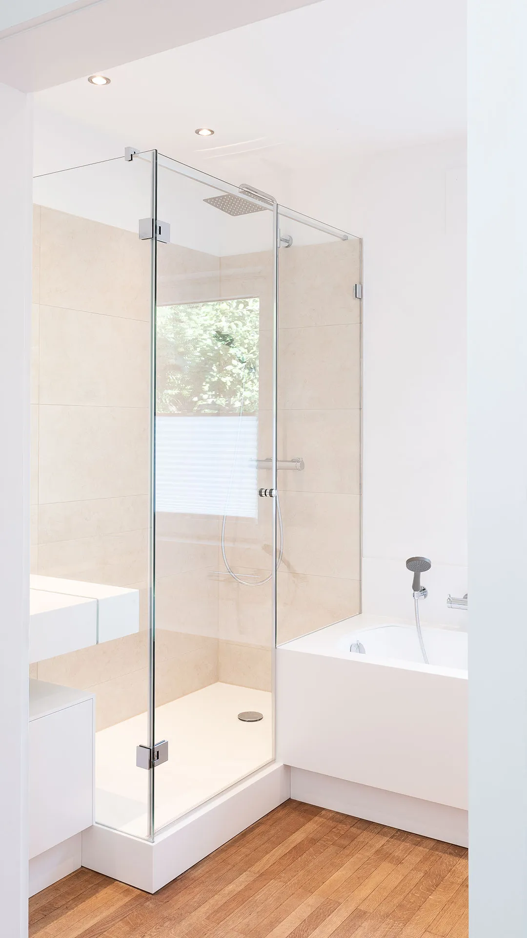 Modern bathroom with glass-enclosed shower, white bathtub, and wooden floor.