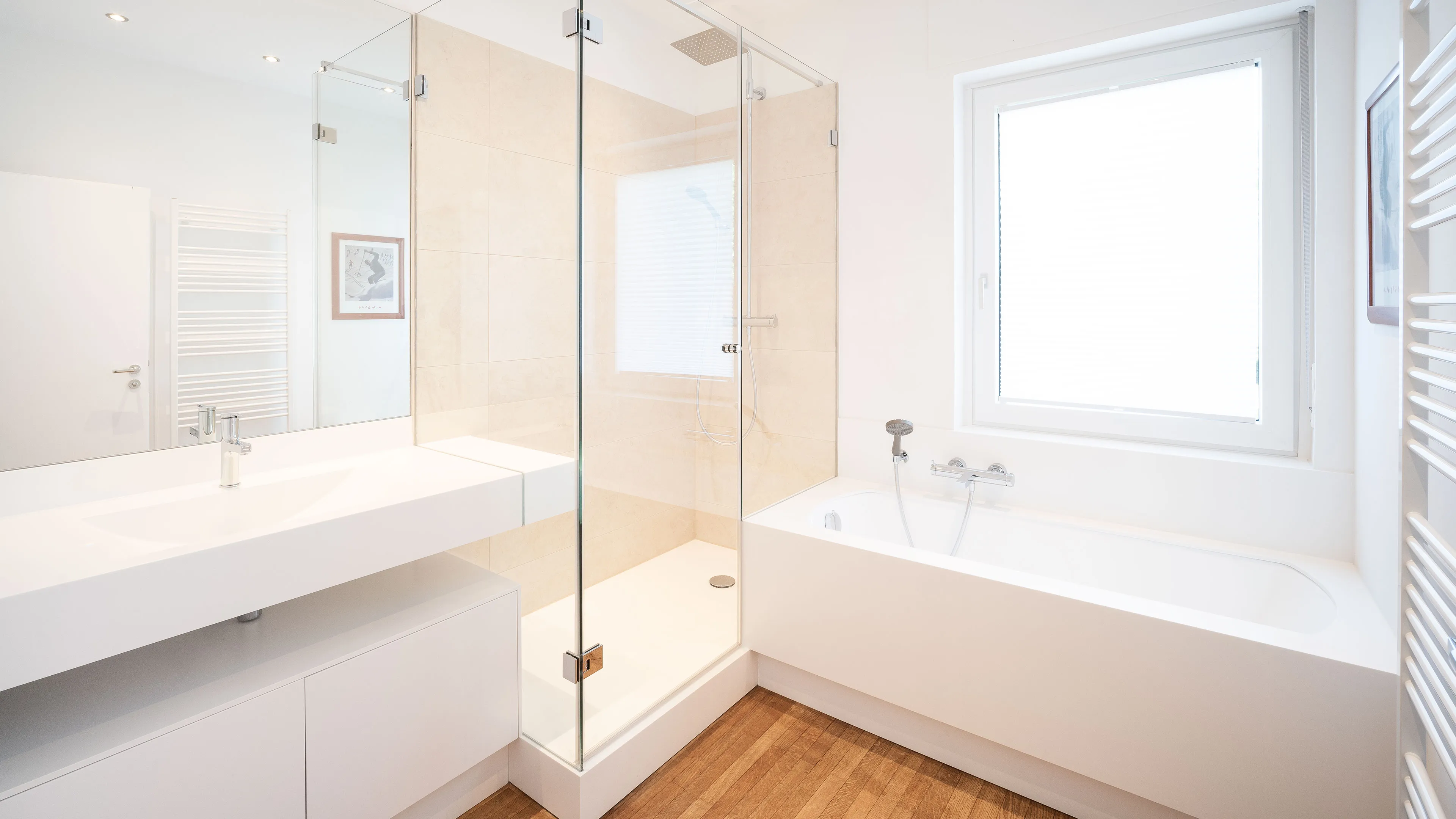 Bright modern bathroom with a glass-enclosed shower, white bathtub under a large window, wood floor, and a white sink with a mirror.