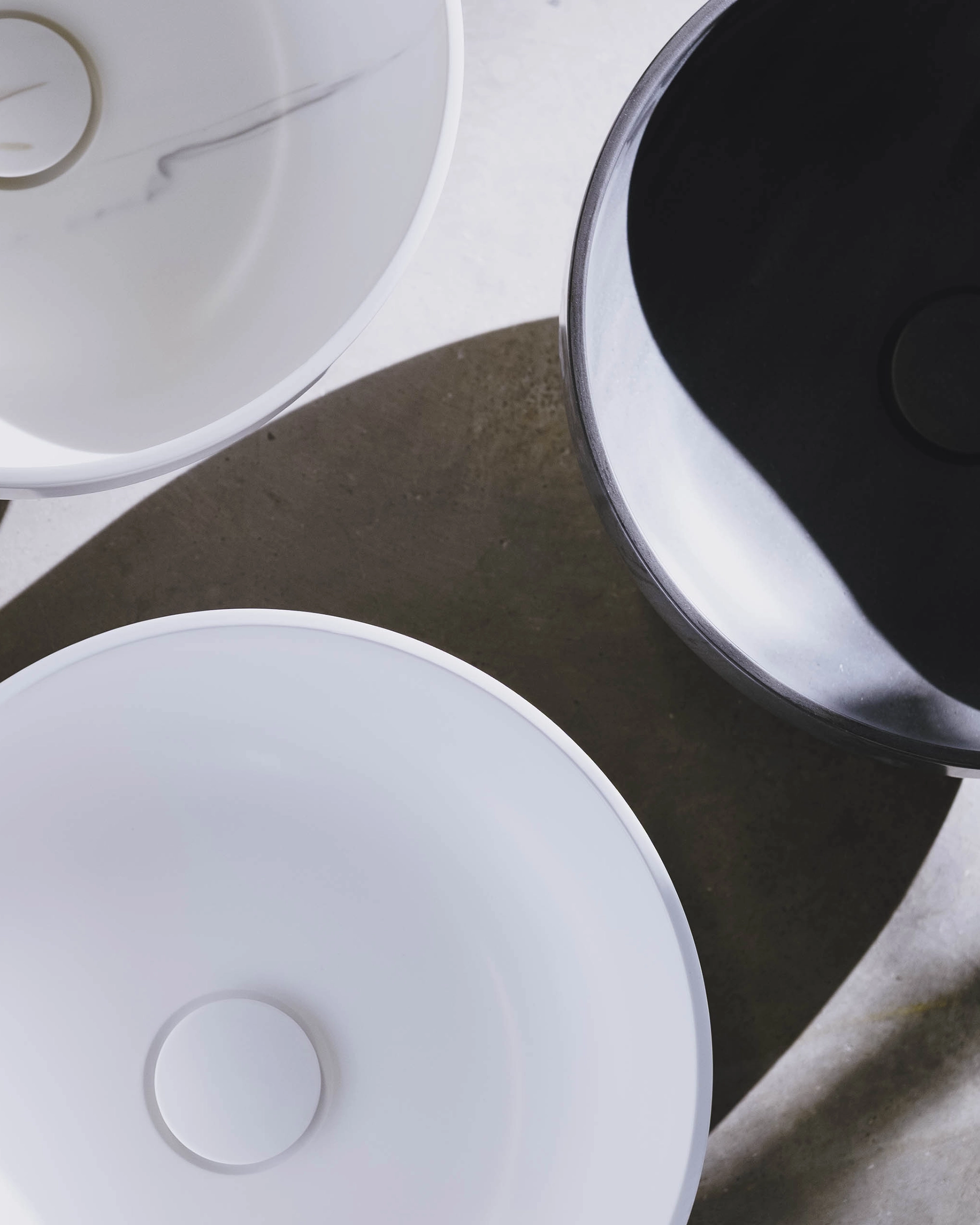 Drei runde Waschbecken in Weiß und Schwarz mit minimalistischer Oberfläche und Schatten darunter.